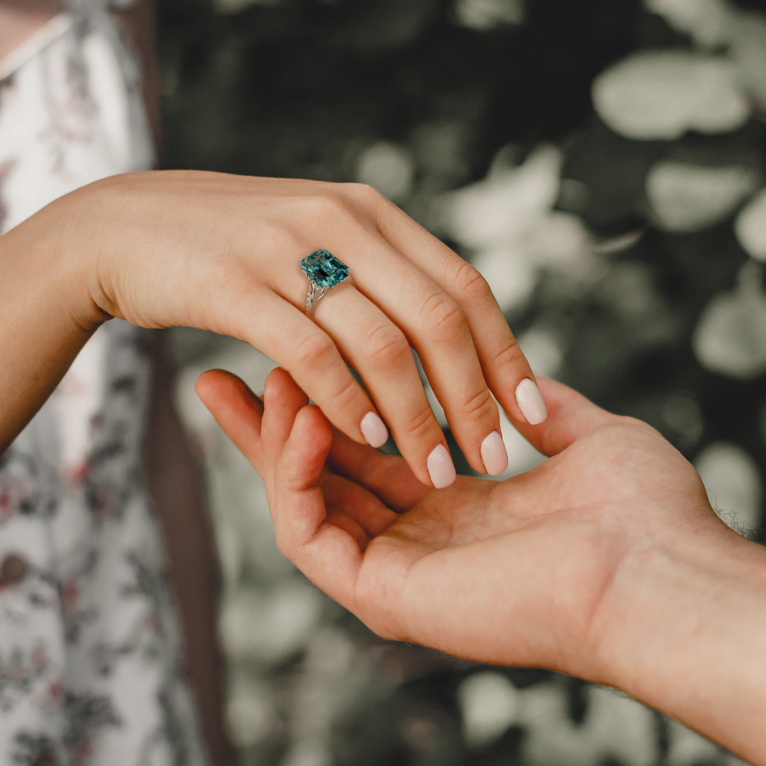 Close-up of two hands; one wears a silver-toned ring with a large teal rectangular gem.