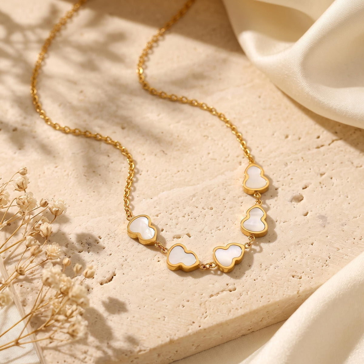 Gold station necklace with five white mother-of-pearl gourd charms laid flat on a stone surface.