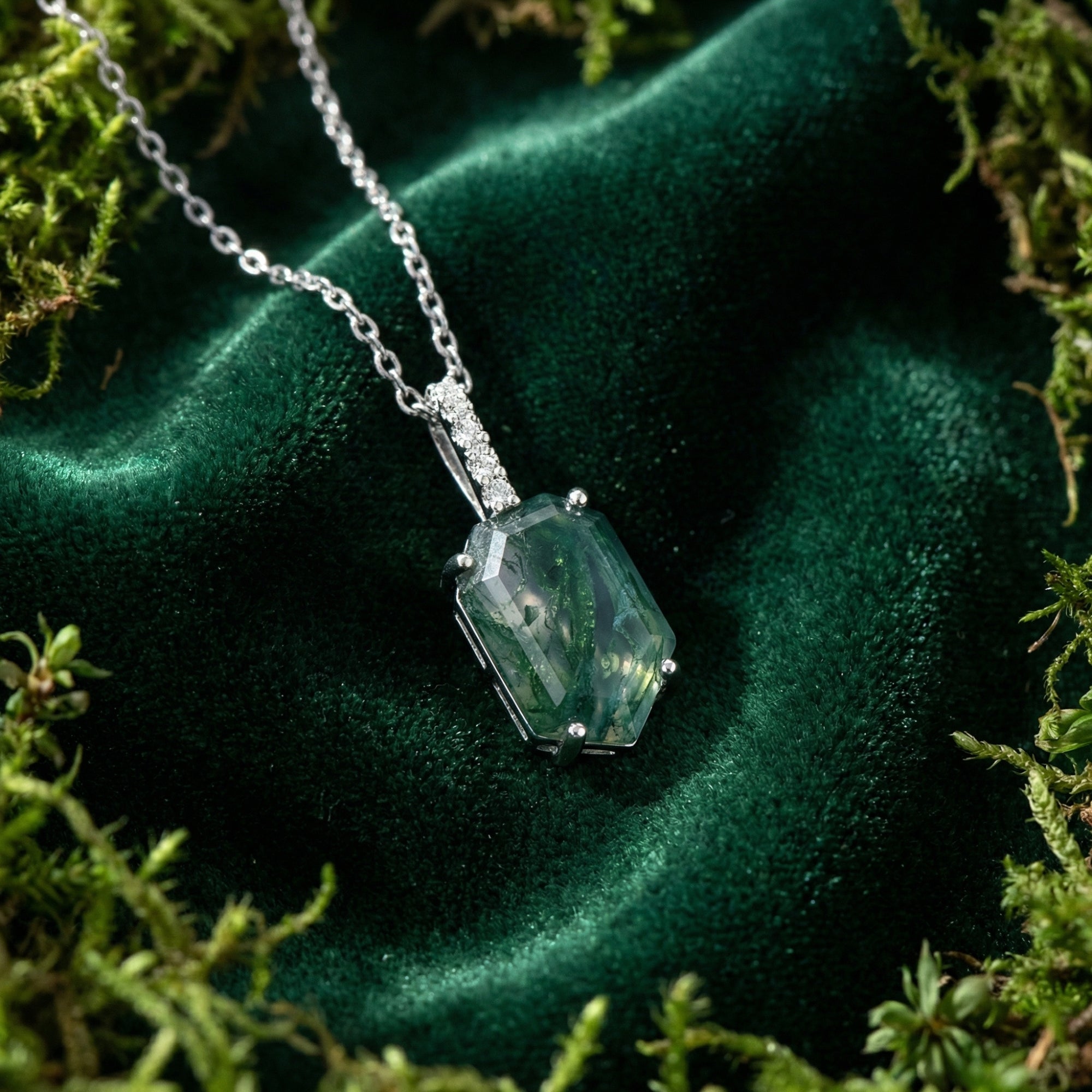 Angled close-up of a coffin cut moss agate column pendant in sterling silver, resting on green velvet and moss.
