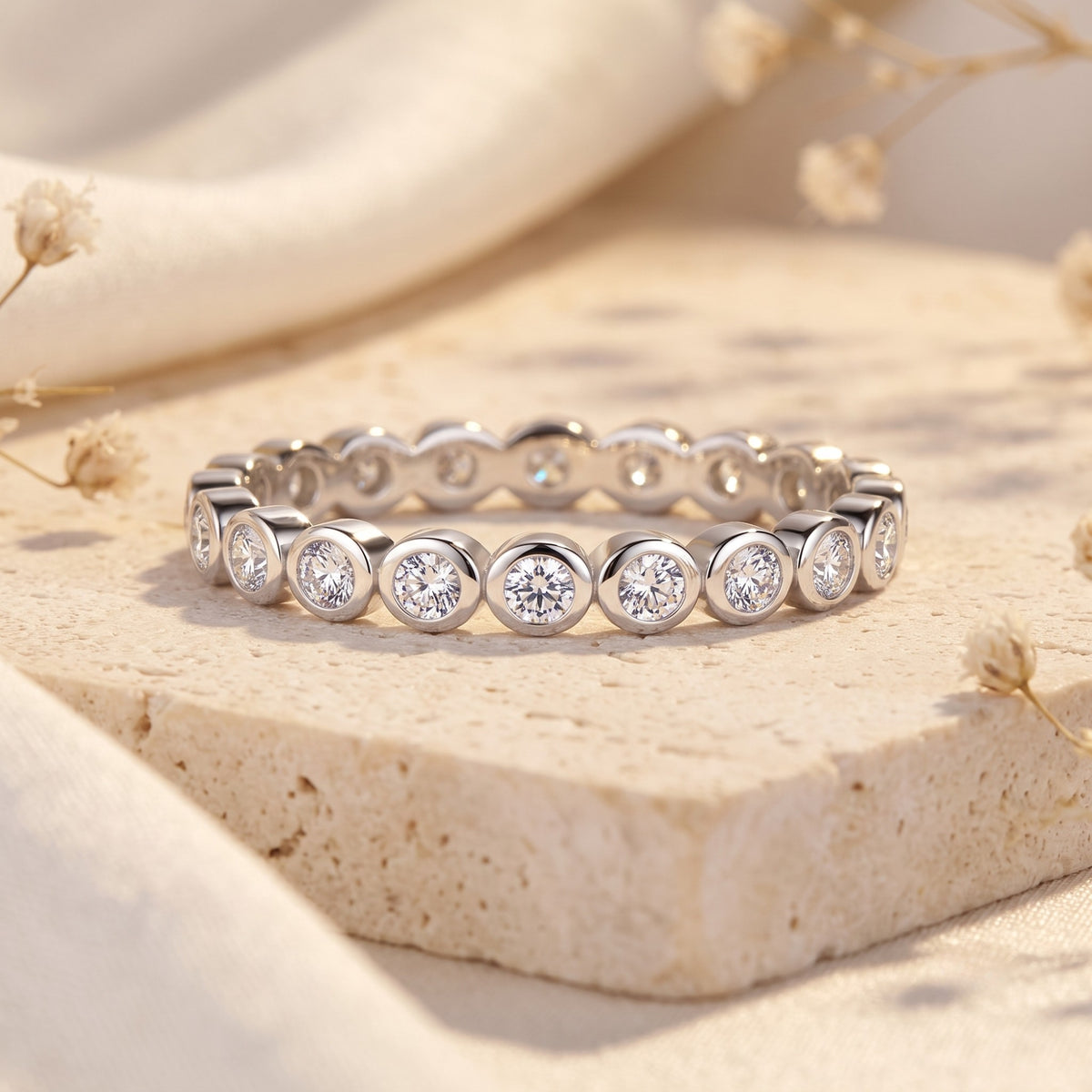 Silver eternity band resting flat on stone, featuring round bezel-set clear gemstones.