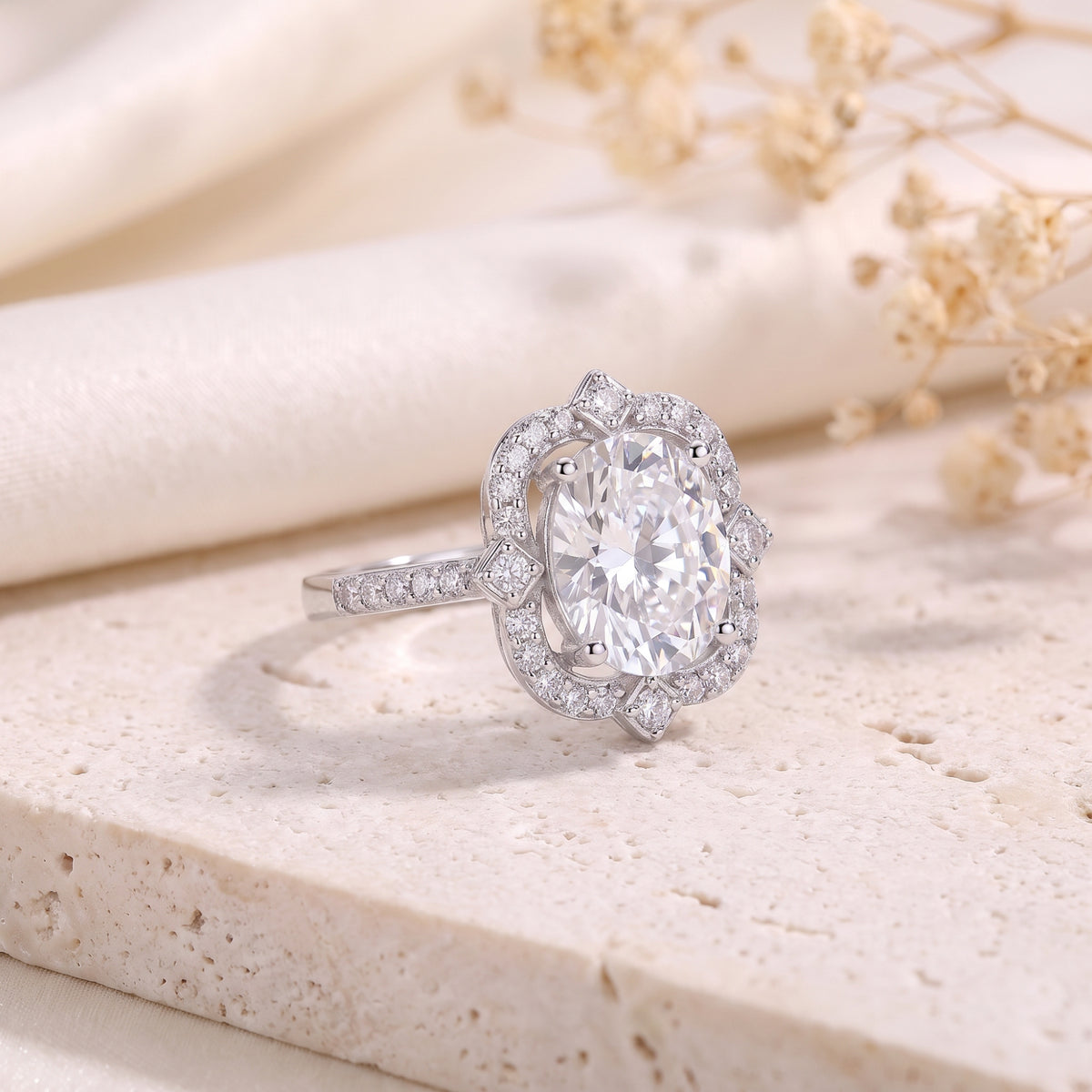 Silver ring with an oval center stone and scalloped halo resting on a stone block.