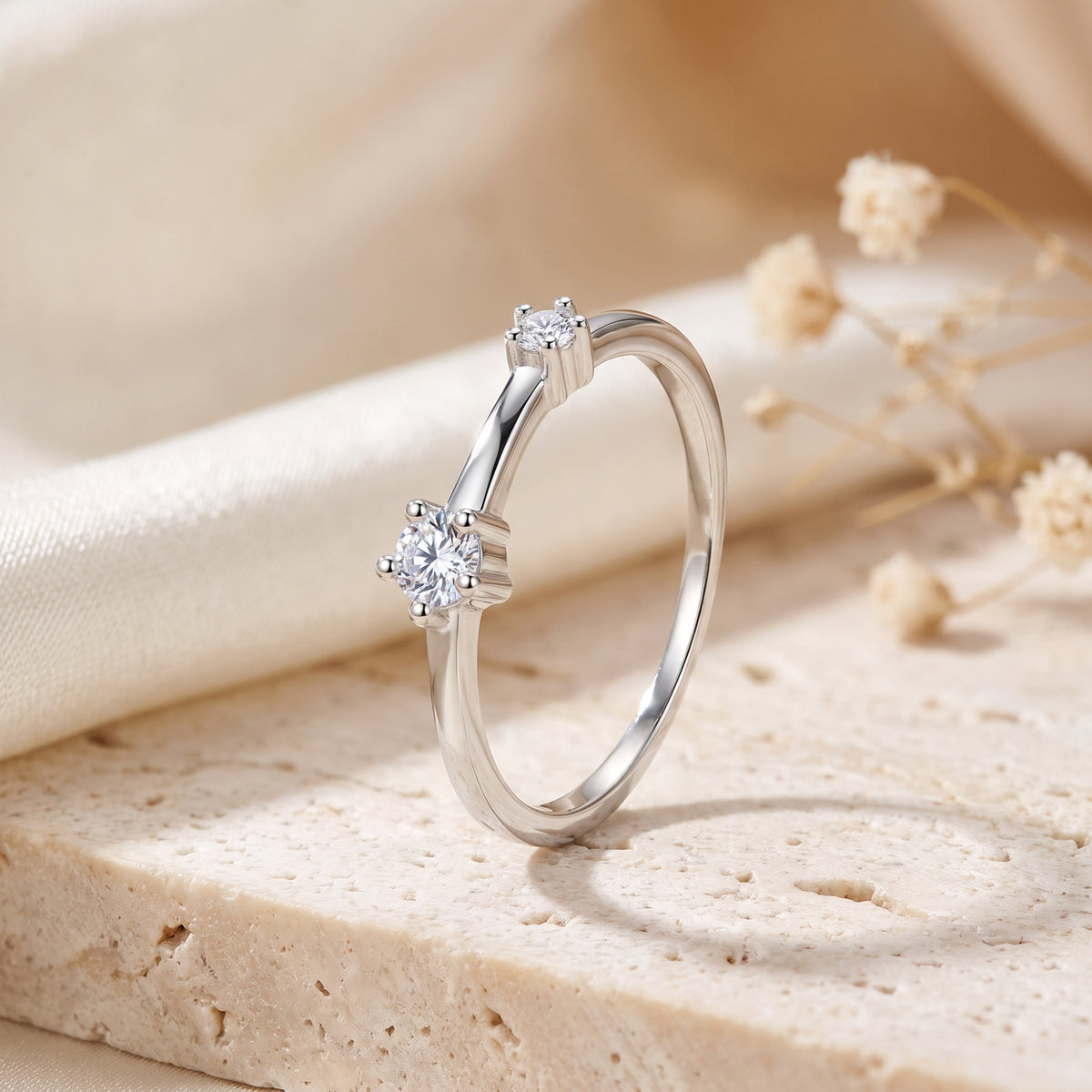 Asymmetric S925 silver bypass ring with two round simulated diamonds on a stone surface.