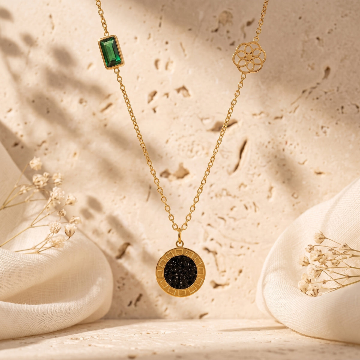 Gold-tone station necklace with a green crystal, openwork floral wheel, and black Greek Key medallion over stone.