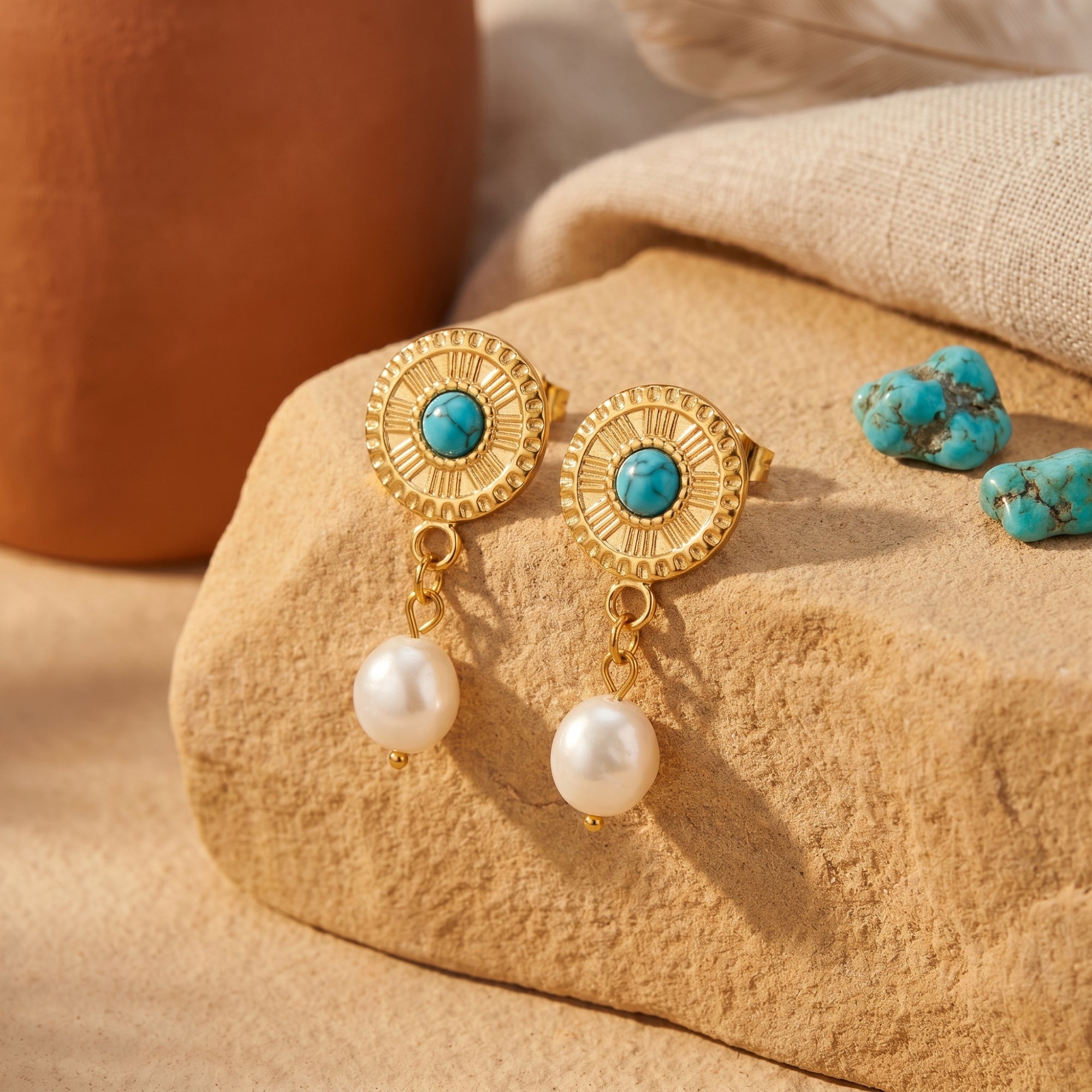Gold turquoise and pearl drop earrings displayed on a desert rock with loose turquoise stones.