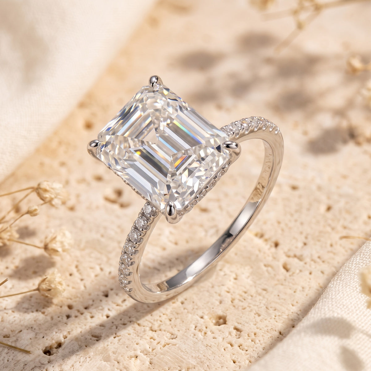 Silver ring featuring a large emerald-cut clear stone and a pavé band on a neutral stone surface.