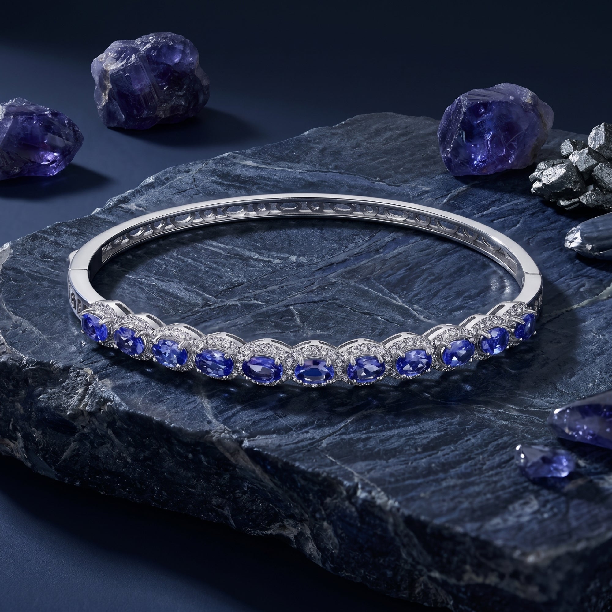 Oval natural tanzanite line bracelet in white gold displayed on dark rock with raw gemstone crystals.