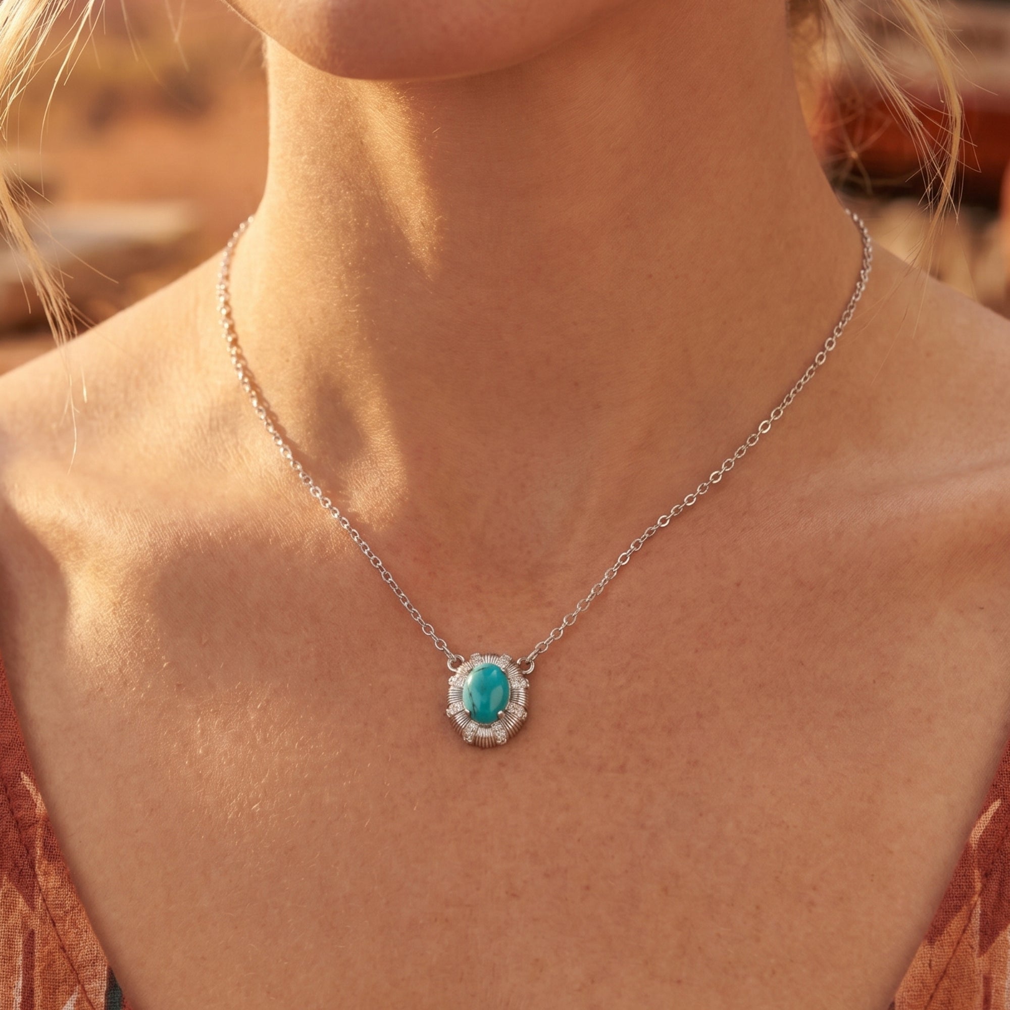 Dainty silver necklace featuring an oval turquoise cabochon in a starburst setting, worn on a woman's neck.