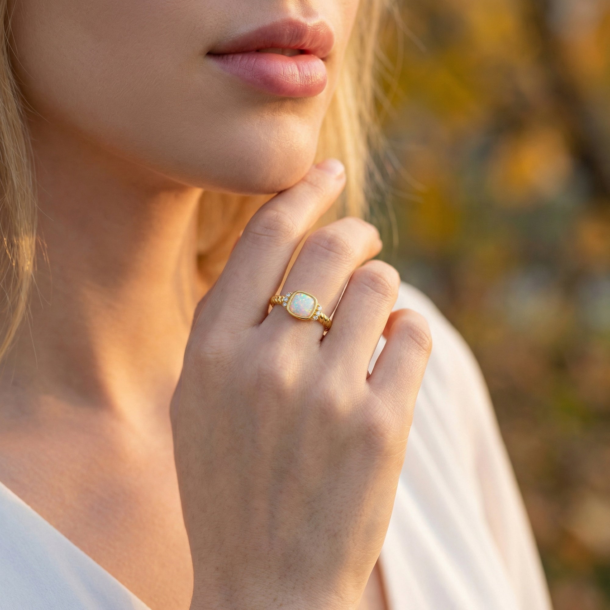 Model wearing the gold-tone cushion-cut white opal ring on her hand against a soft outdoor background.