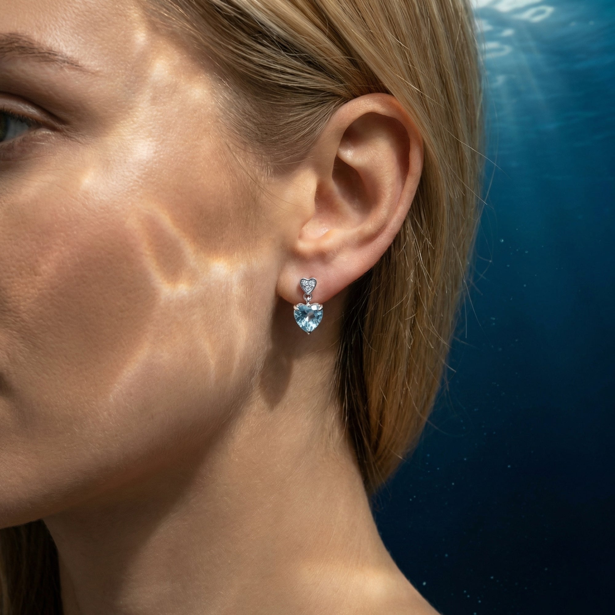 Model wearing a heart-cut aquamarine drop earring in 18K white gold with light patterns on her face.