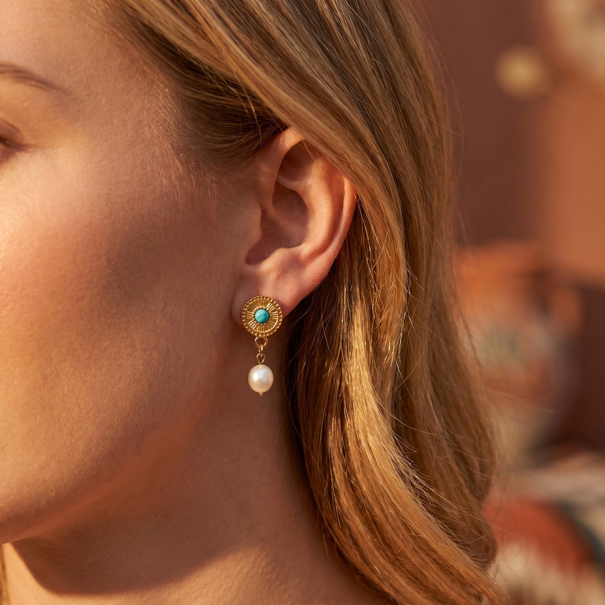 Close-up of a woman wearing a gold Maricopa turquoise drop earring with a white pearl accent.