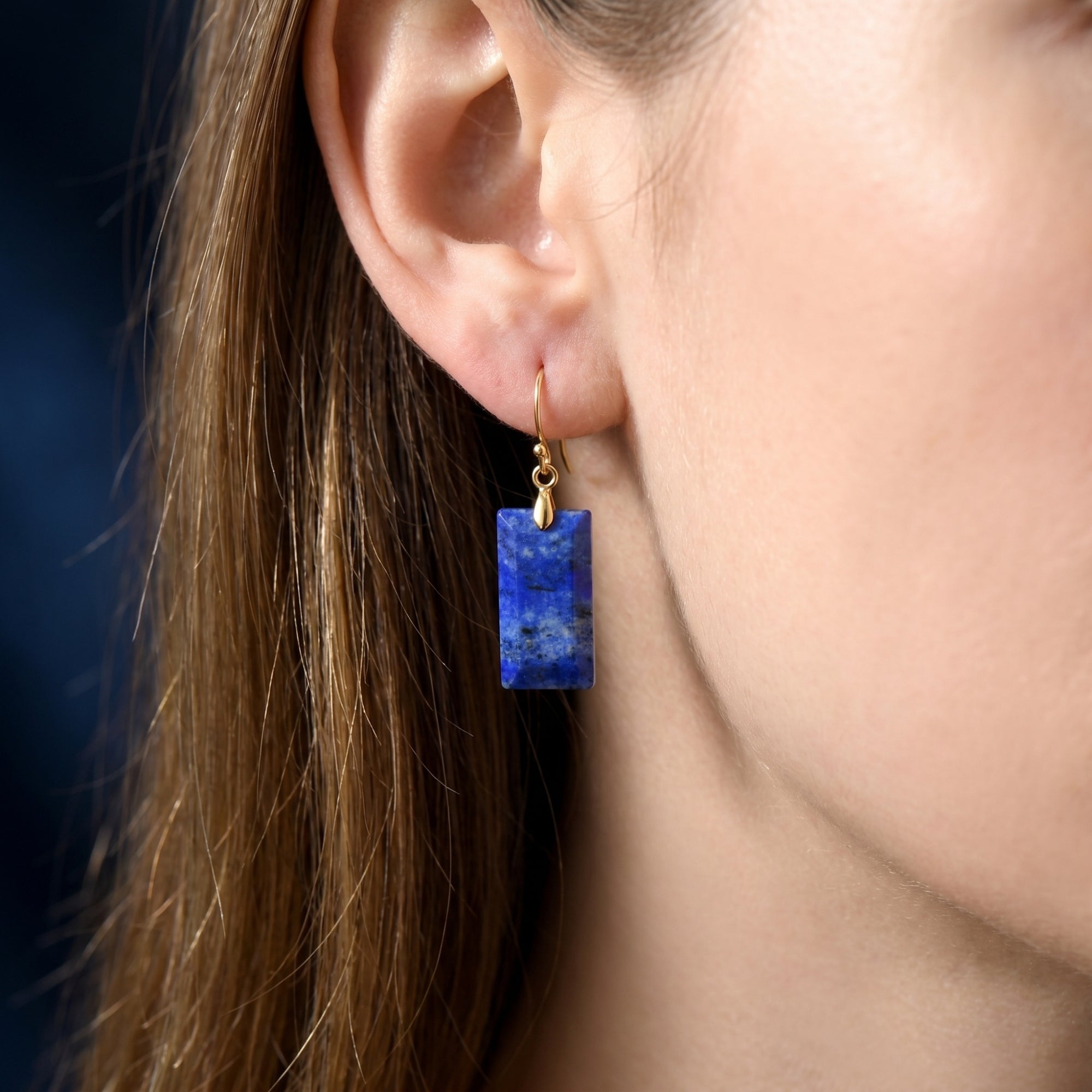Close-up of a model wearing a rectangular natural lapis lazuli drop earring with a gold hook.