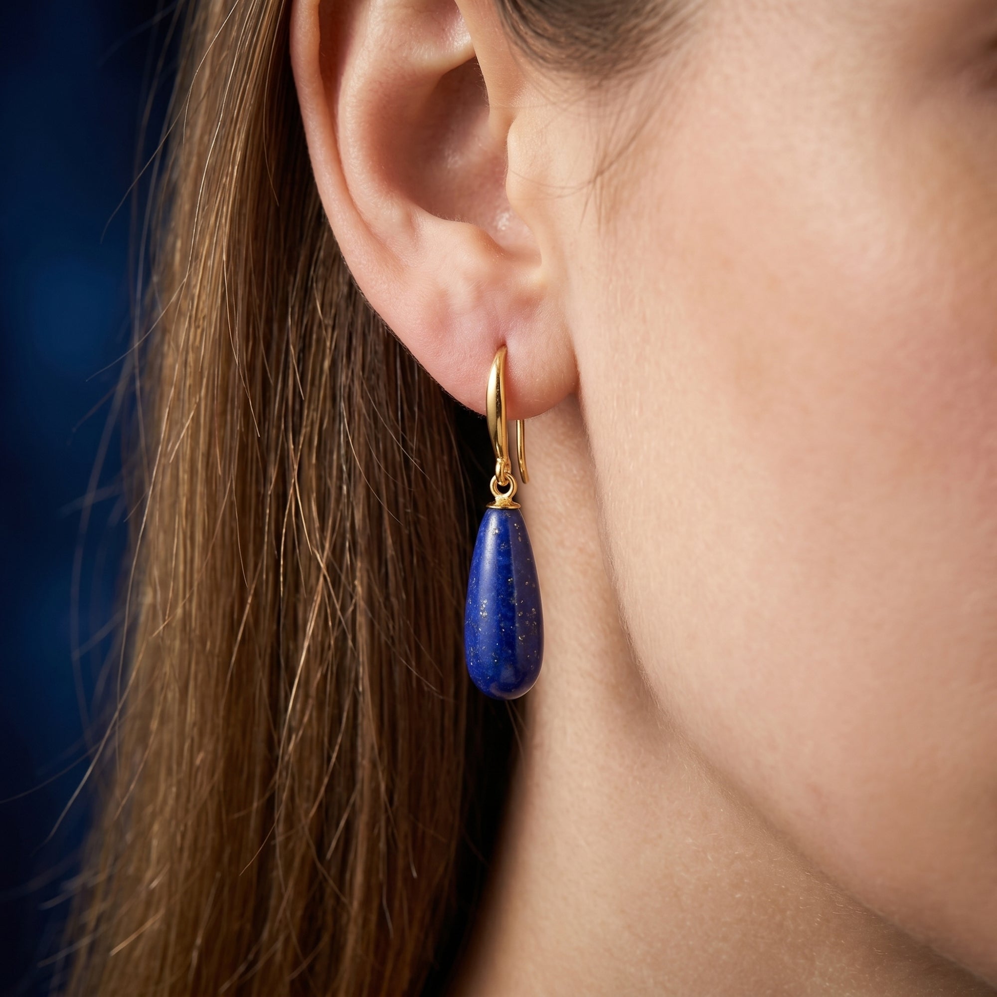 A woman wearing a pear-shaped natural lapis lazuli drop earring with an 18K gold plated hook.