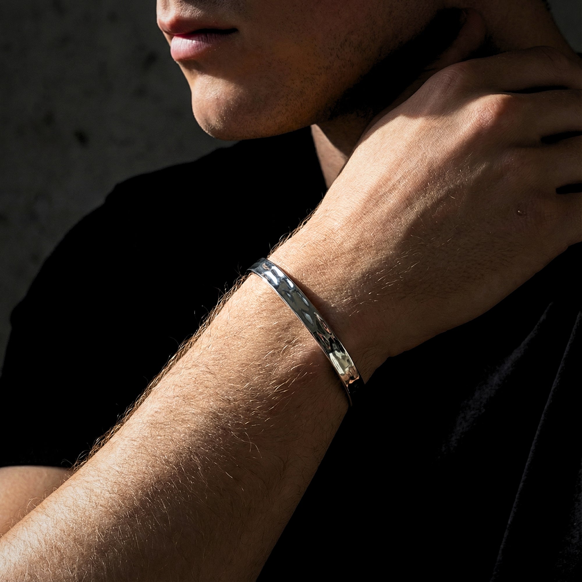 Men's silver hammered stainless steel cuff bangle worn on a wrist, showing the polished finish.