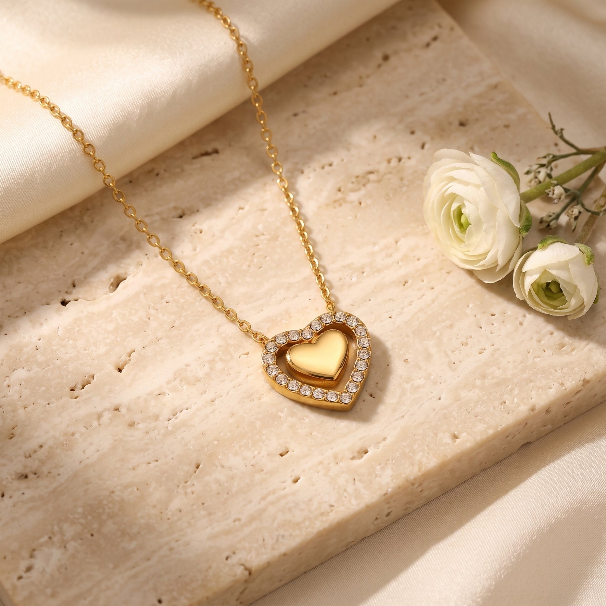 Close-up of an 18K gold PVD finished double heart necklace with round cut simulated diamonds on a stone surface.