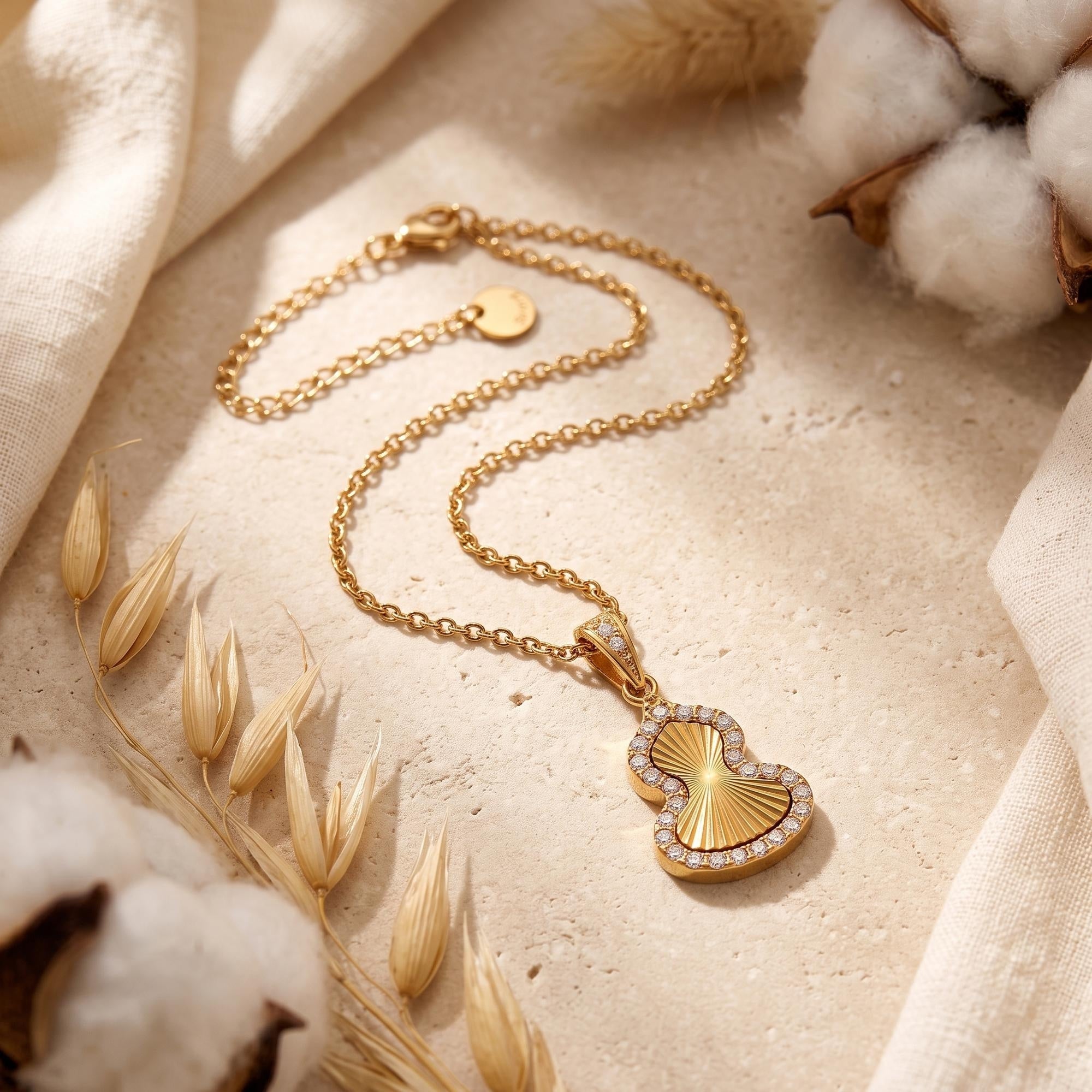 Gold gourd pendant necklace with cubic zirconia halo on textured surface with dried botanicals.