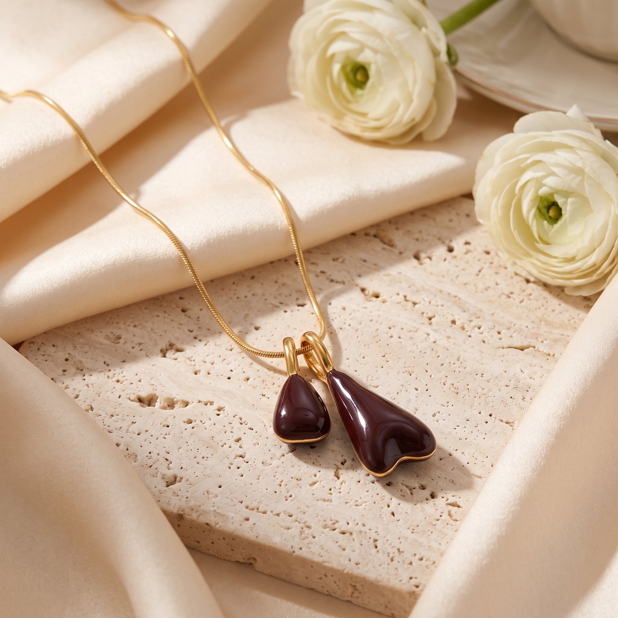 Detail of the Marais gold pendant necklace showing the high-gloss burgundy double drops on a textured stone.