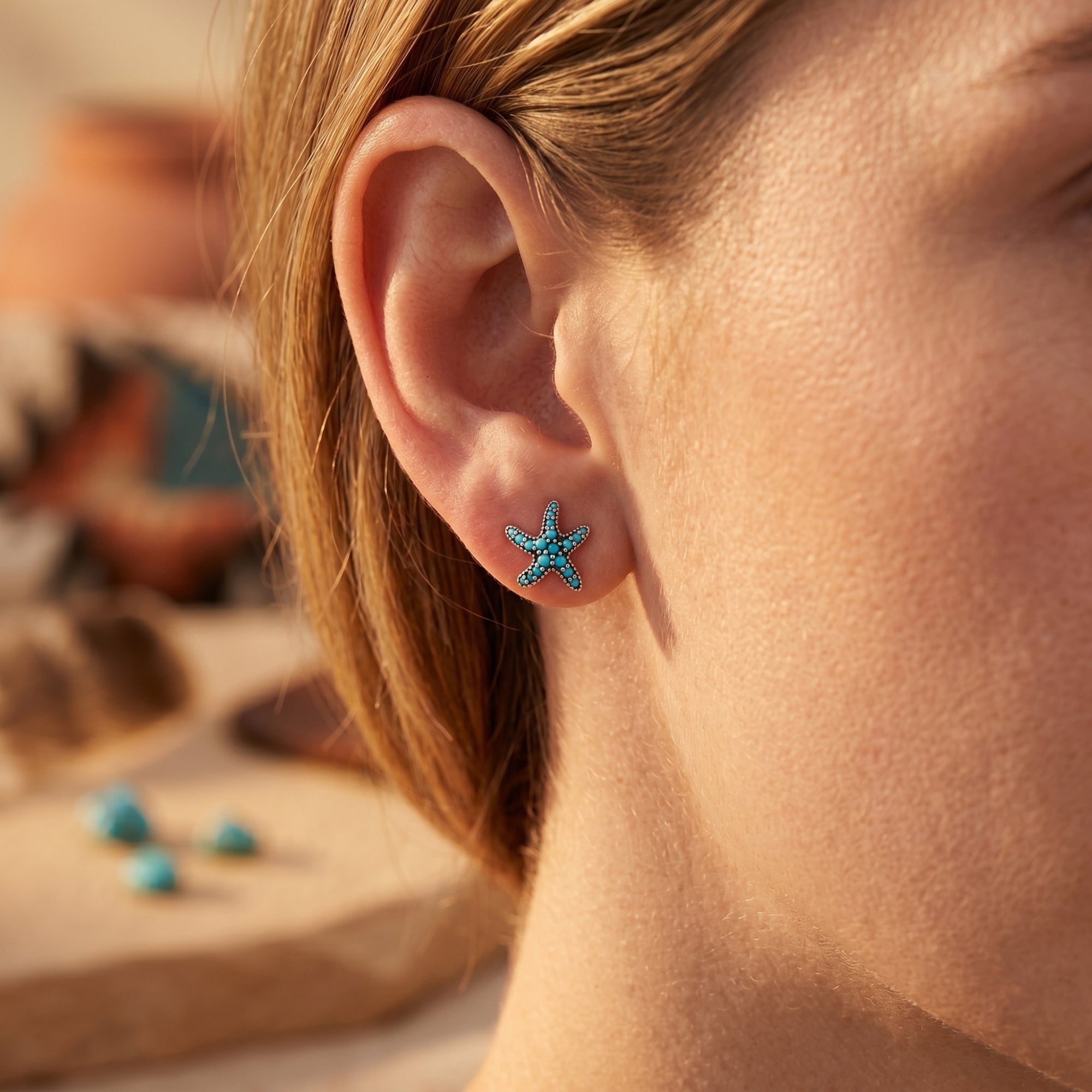 Woman wearing a sterling silver starfish stud earring with round turquoise stones in a lifestyle setting.