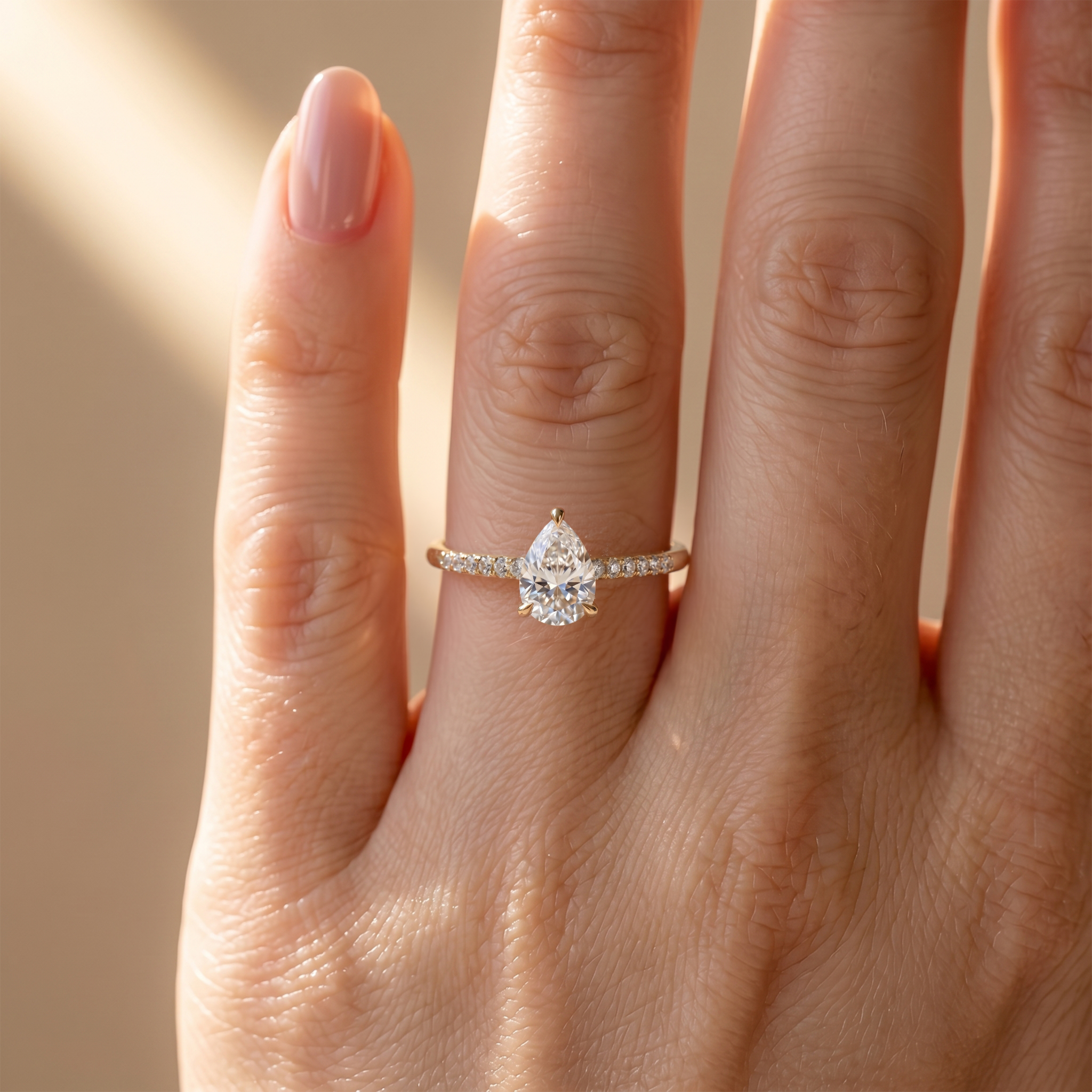A yellow gold pear-shaped moissanite ring with a sparkling pavé band worn on a woman's finger.