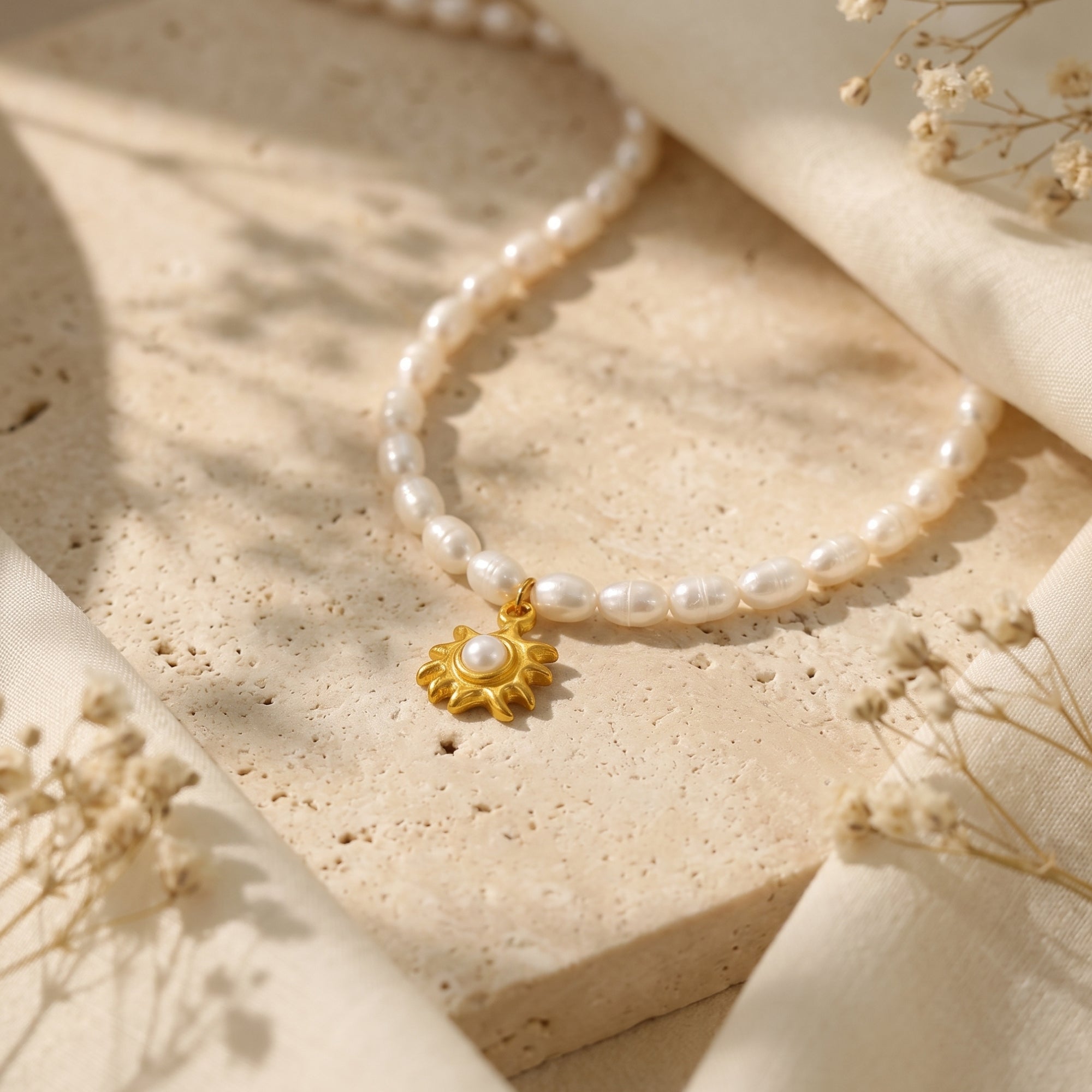 Close-up of a gold sunburst pendant and freshwater pearls on a neutral stone background with soft shadows.