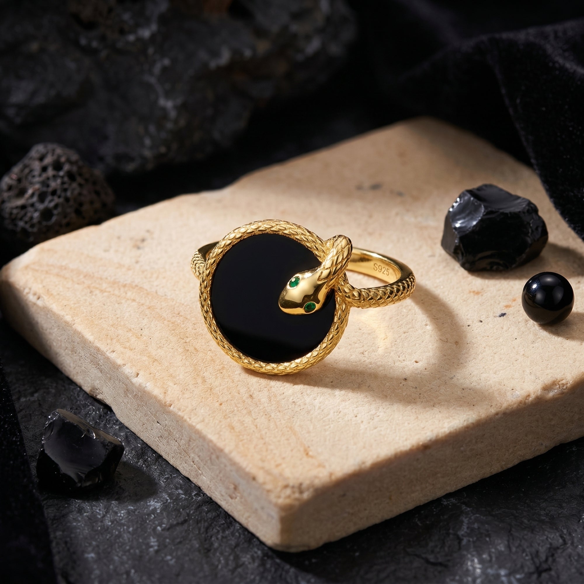 Detailed view of the Regalia gold plated silver snake ring with a circular black onyx inlay and green eyes.