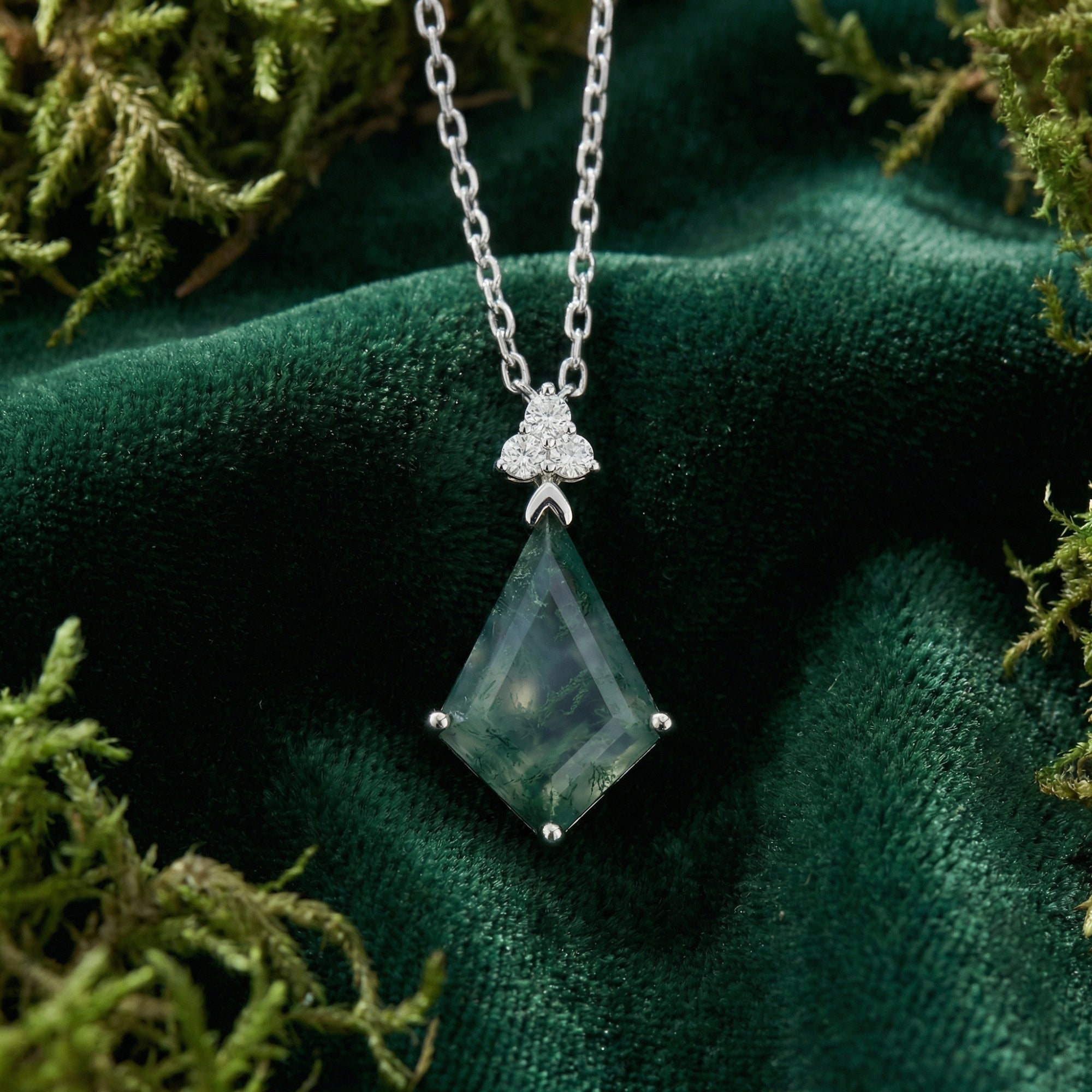 Close-up of a kite cut moss agate pendant with sterling silver setting and accent stones on green velvet.