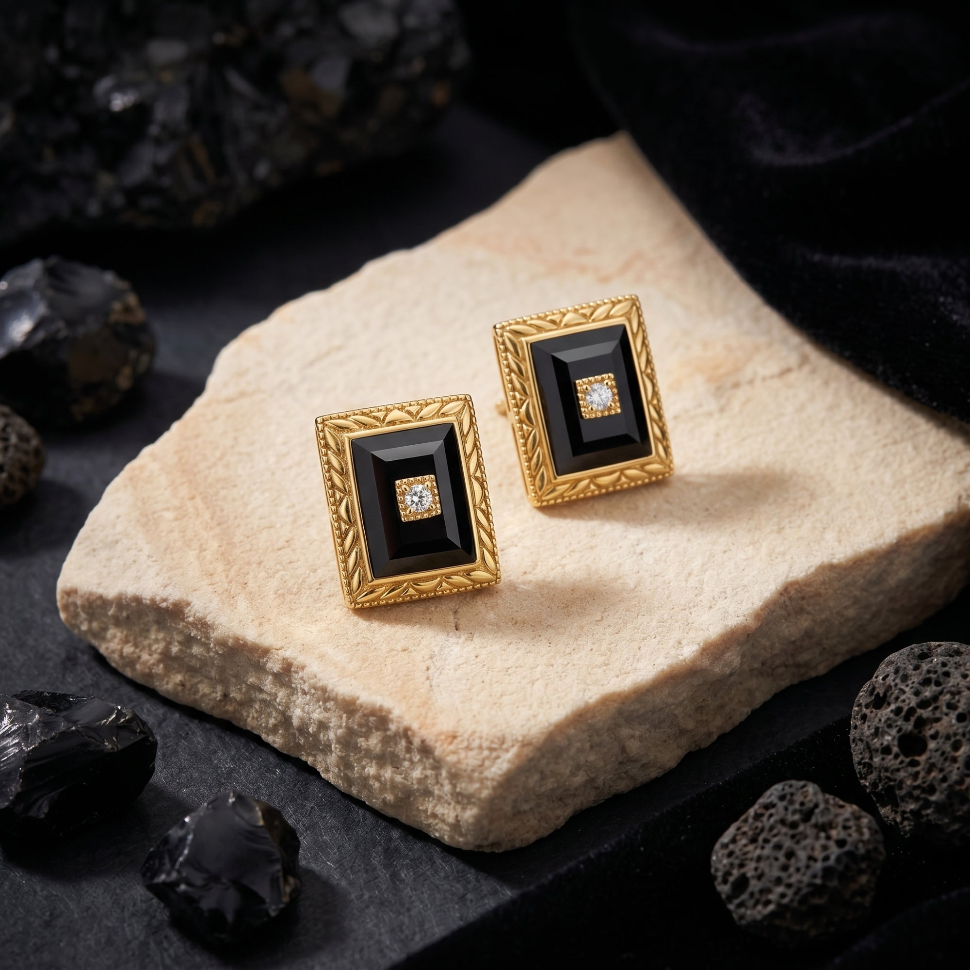 Pair of yellow gold square-cut onyx earrings with textured borders displayed on a light stone and black rock background.