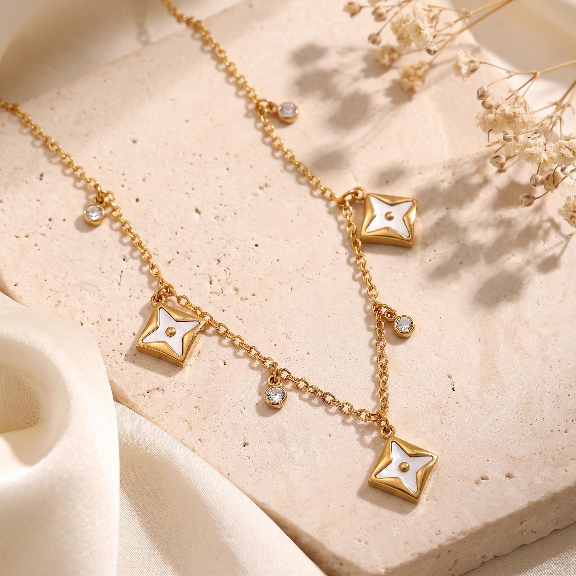 Close-up of gold star pendants with white inlays and brilliant-cut crystals on a textured stone surface.