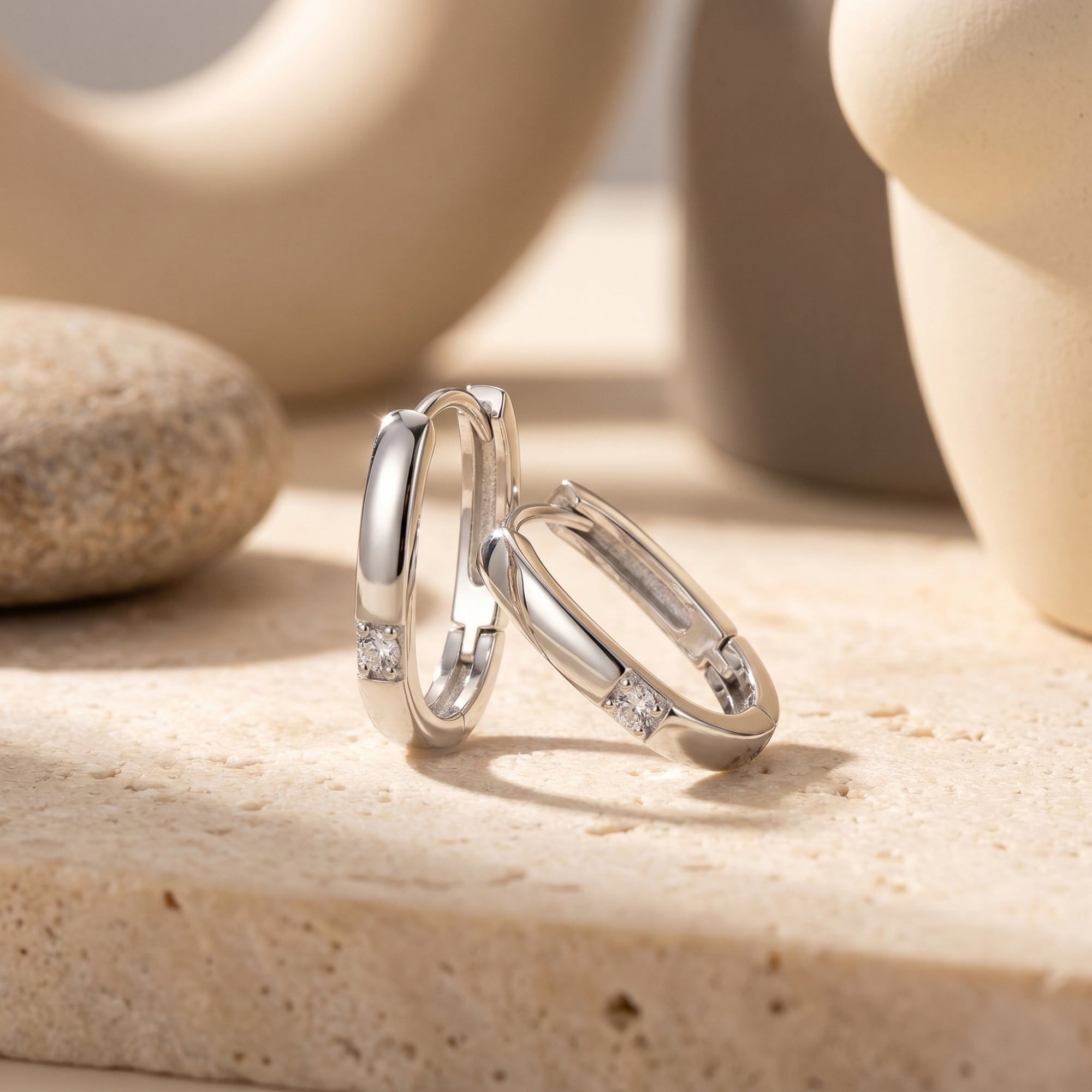Macro view of white gold huggie hoop earrings showing the round lab moissanite stone and polished metal finish.