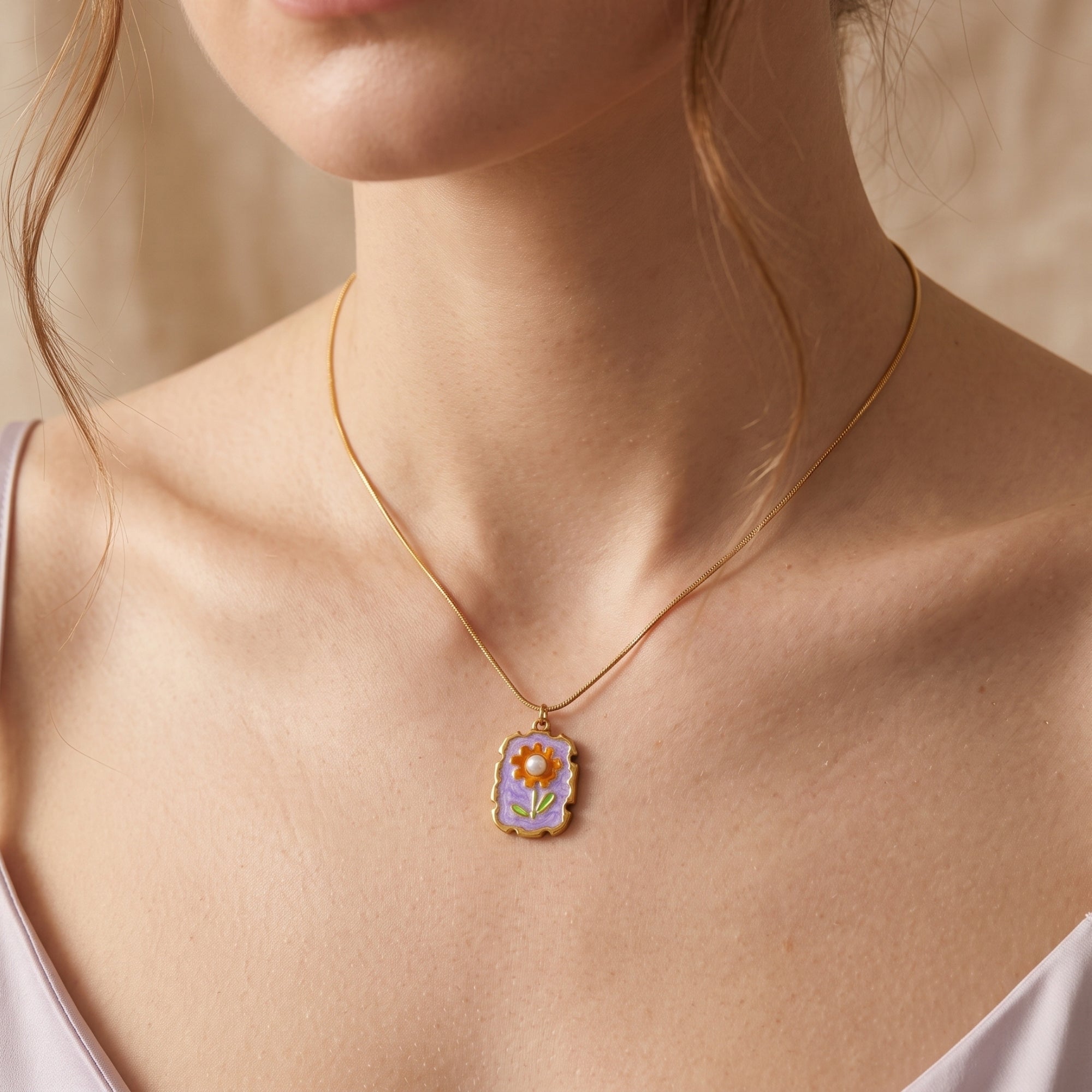 Gold floral statement necklace with purple enamel and pearl worn by a model against a soft neutral background.