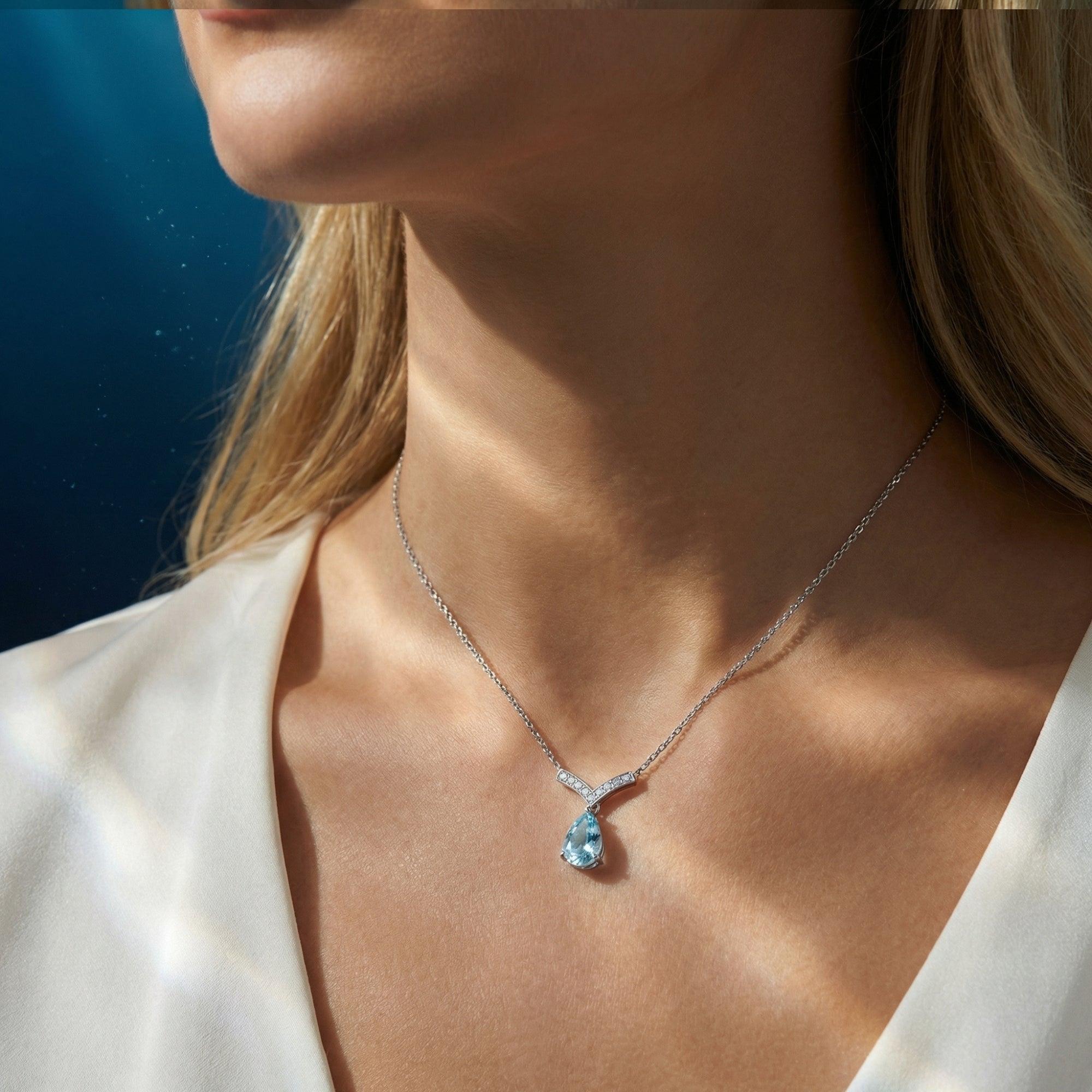 Pear cut aquamarine and platinum necklace worn by a model, styled with a white V-neck blouse.