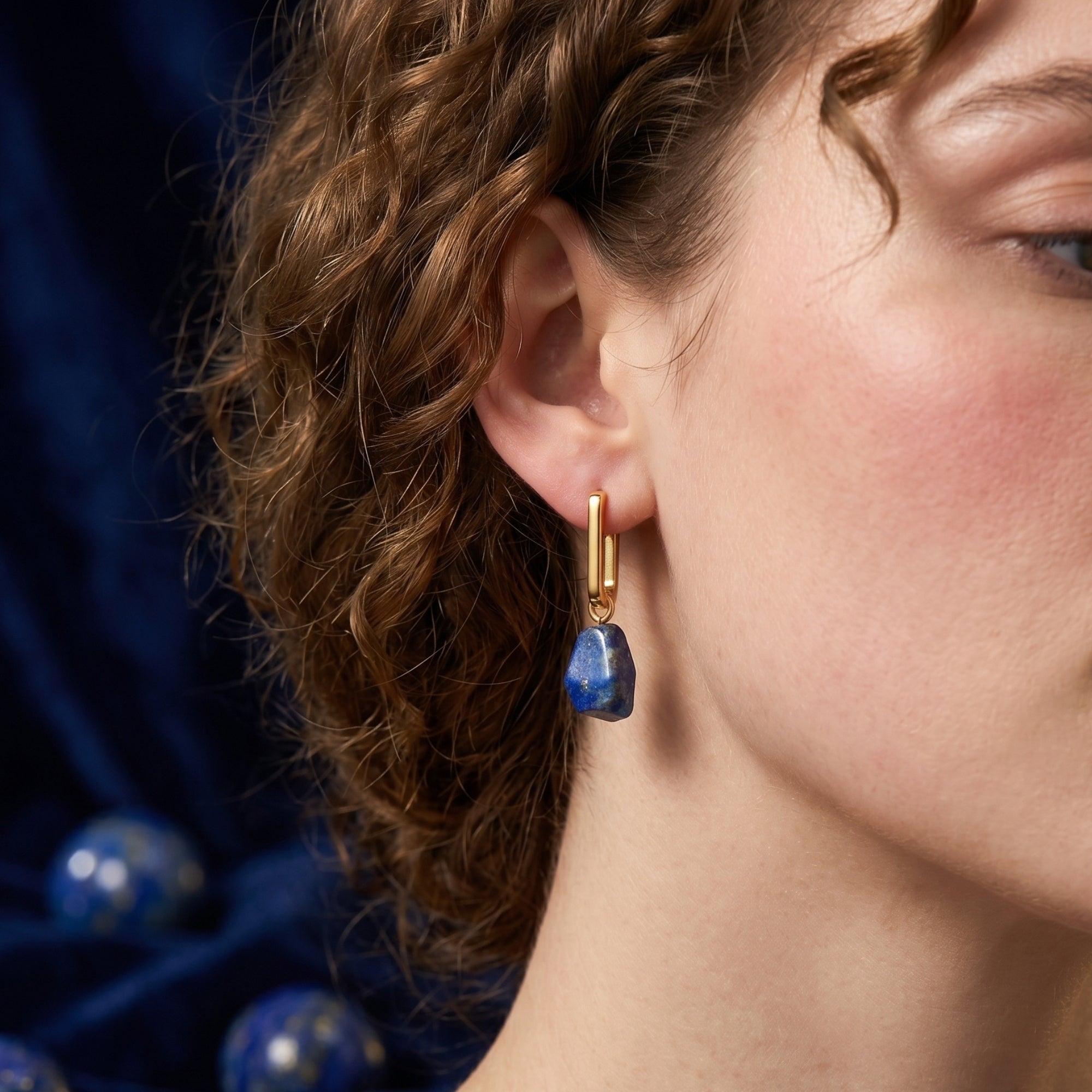 Profile view of a model wearing the Cybele gold-plated earrings with natural blue lapis lazuli irregular drops.