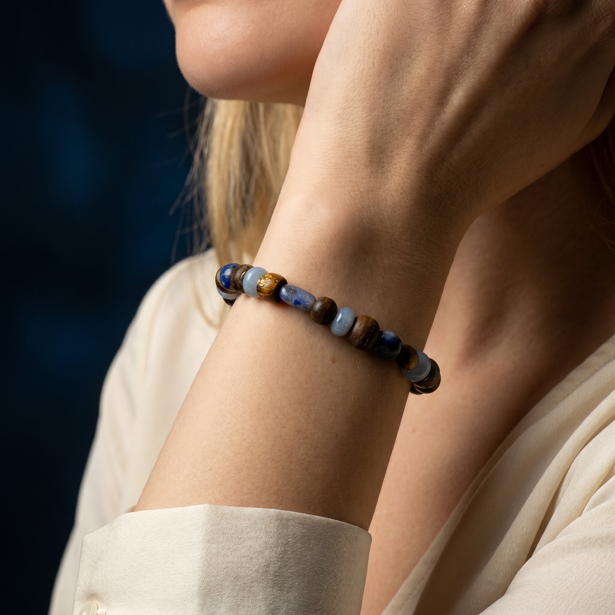 Woman in a cream shirt wearing the Stargazer Natural Lapis Bracelet with round lapis beads and gold plated charm.