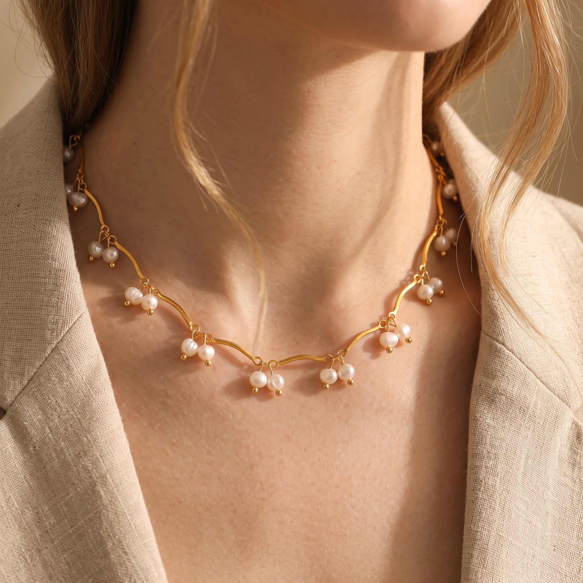 Editorial view of a model wearing the Aurendra gold pearl necklace with a beige linen blazer.