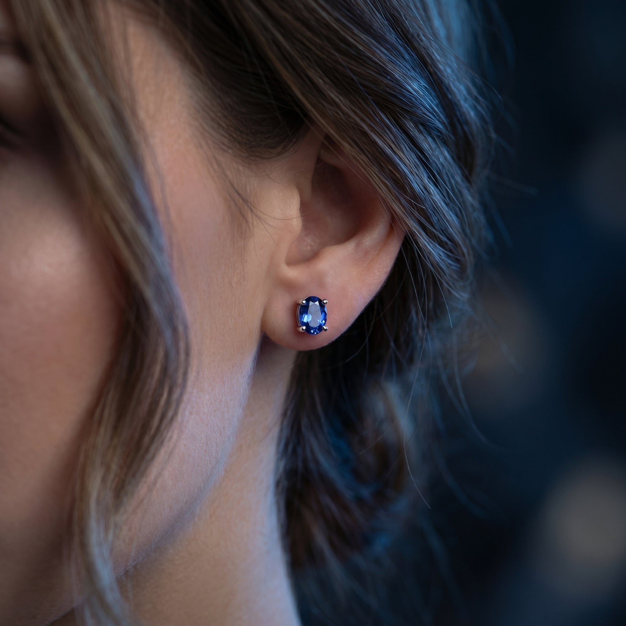 Close-up view of an 18K white gold oval natural tanzanite earring worn on a woman's ear.