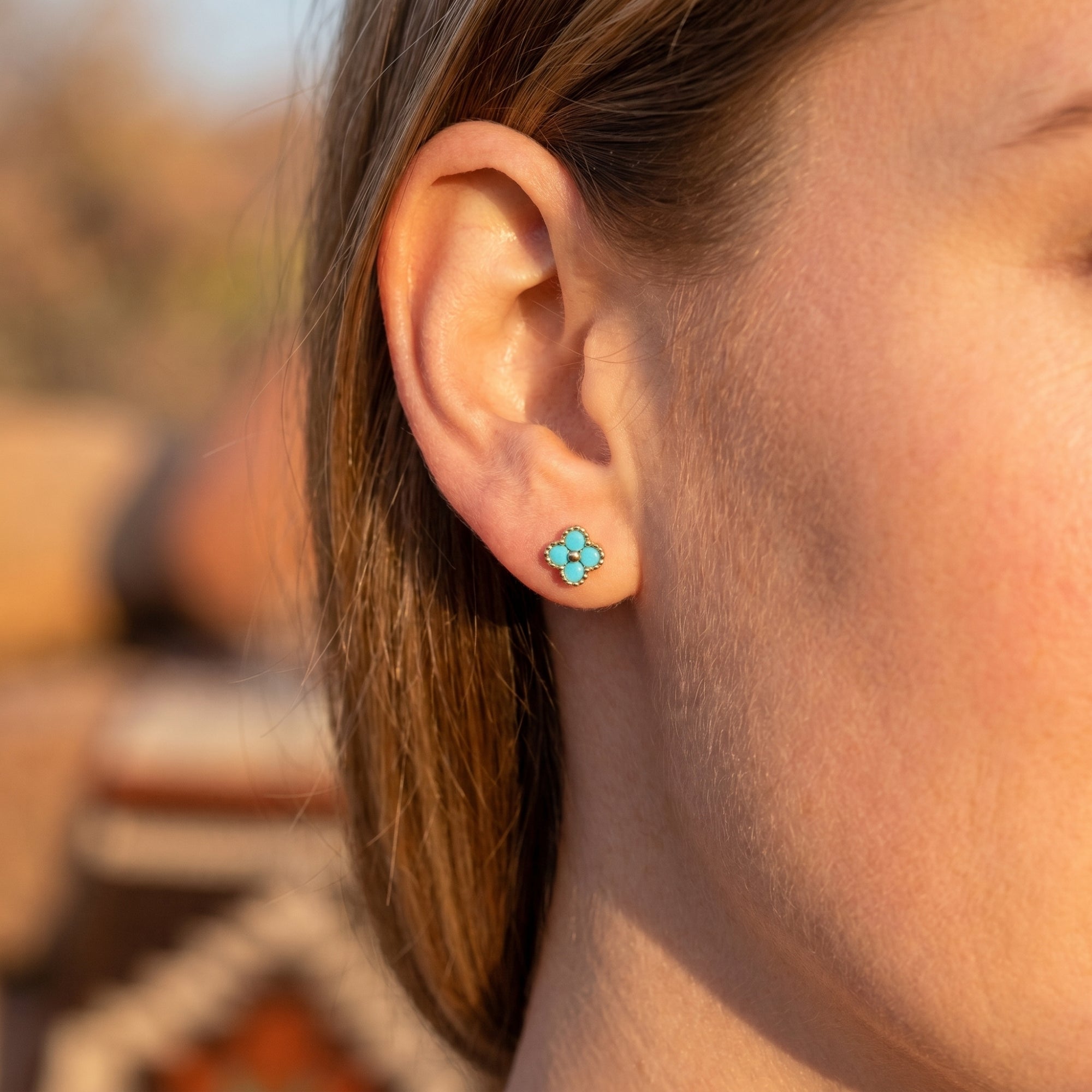 Side view of a gold vermeil turquoise clover stud earring worn on a model's ear in natural outdoor light.