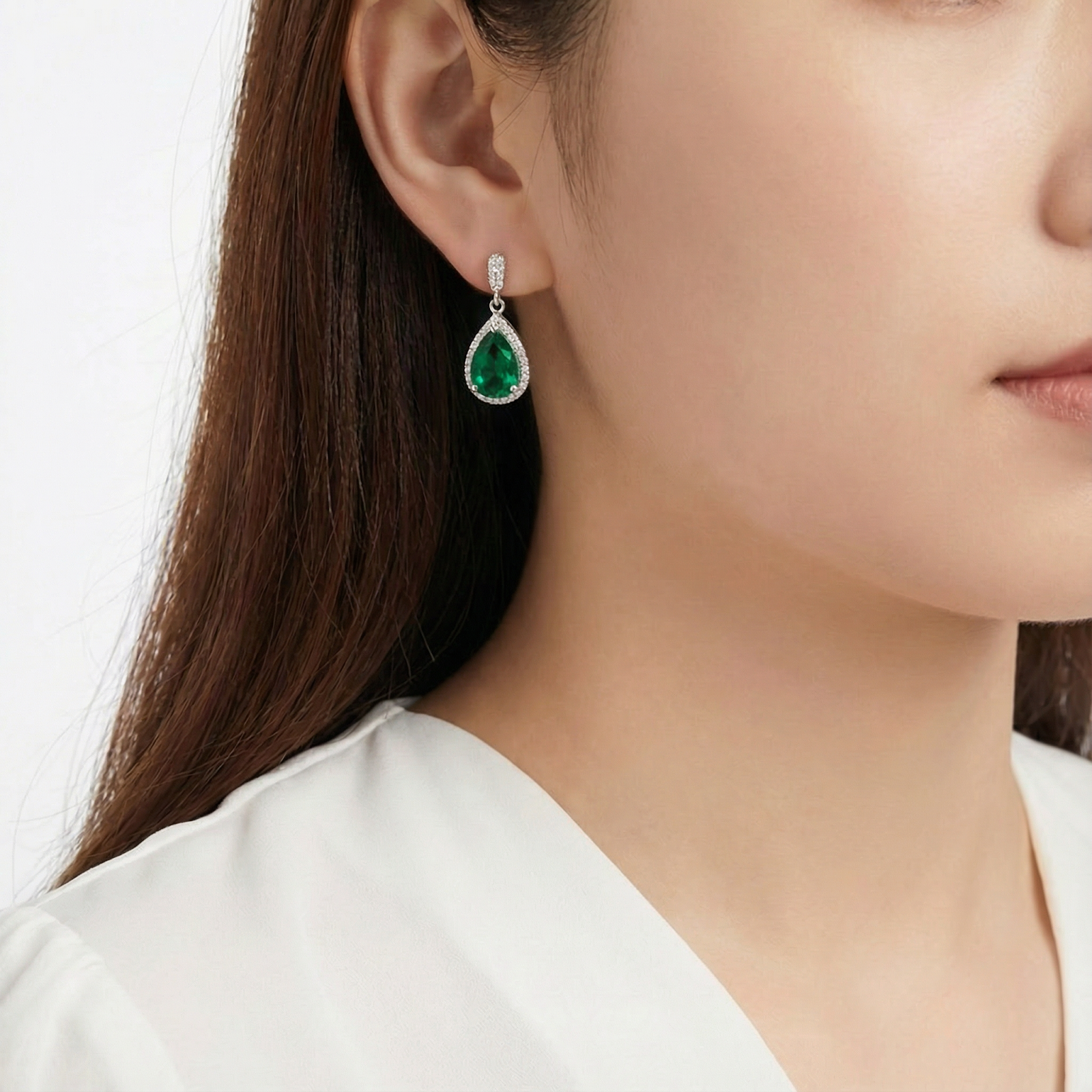 Woman wearing a sterling silver teardrop drop earring with a vibrant green simulated emerald stone.