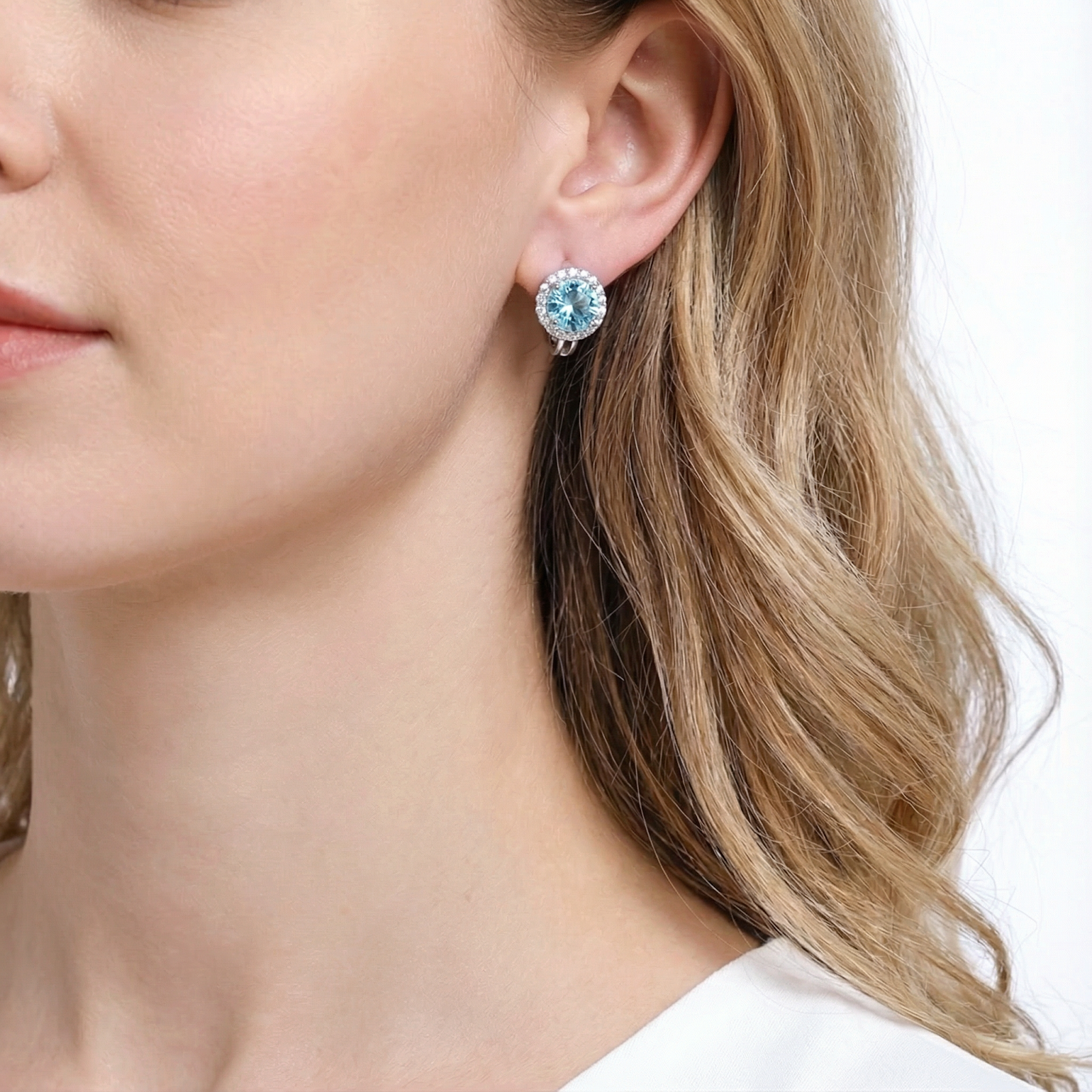 Close-up of a sterling silver halo drop earring with a round cut light blue simulated aquamarine on a model.