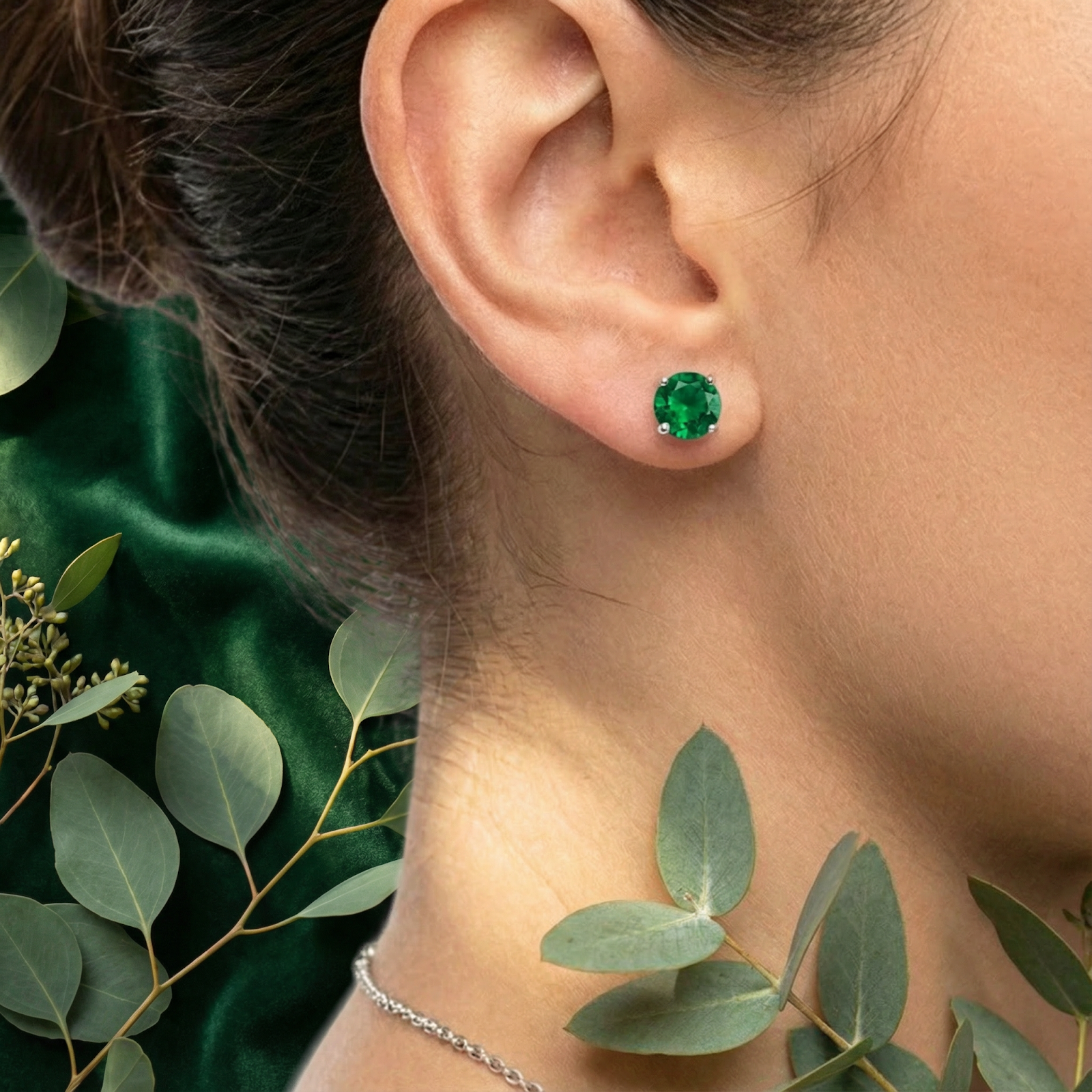 Woman wearing a round-cut simulated emerald stud earring in sterling silver, styled with eucalyptus leaves.