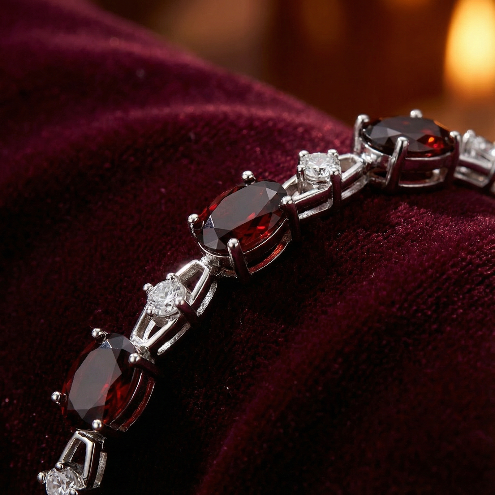 Macro view of oval cut simulated garnets and round white stones in a sterling silver helix bracelet.