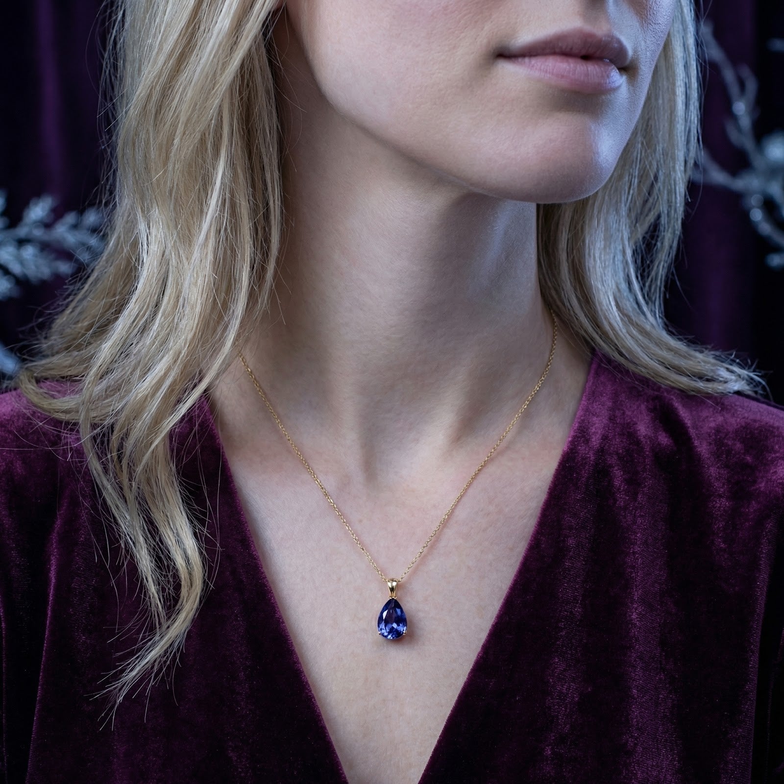 Model wearing the pear-cut simulated tanzanite necklace in 18K gold vermeil with a maroon velvet top.