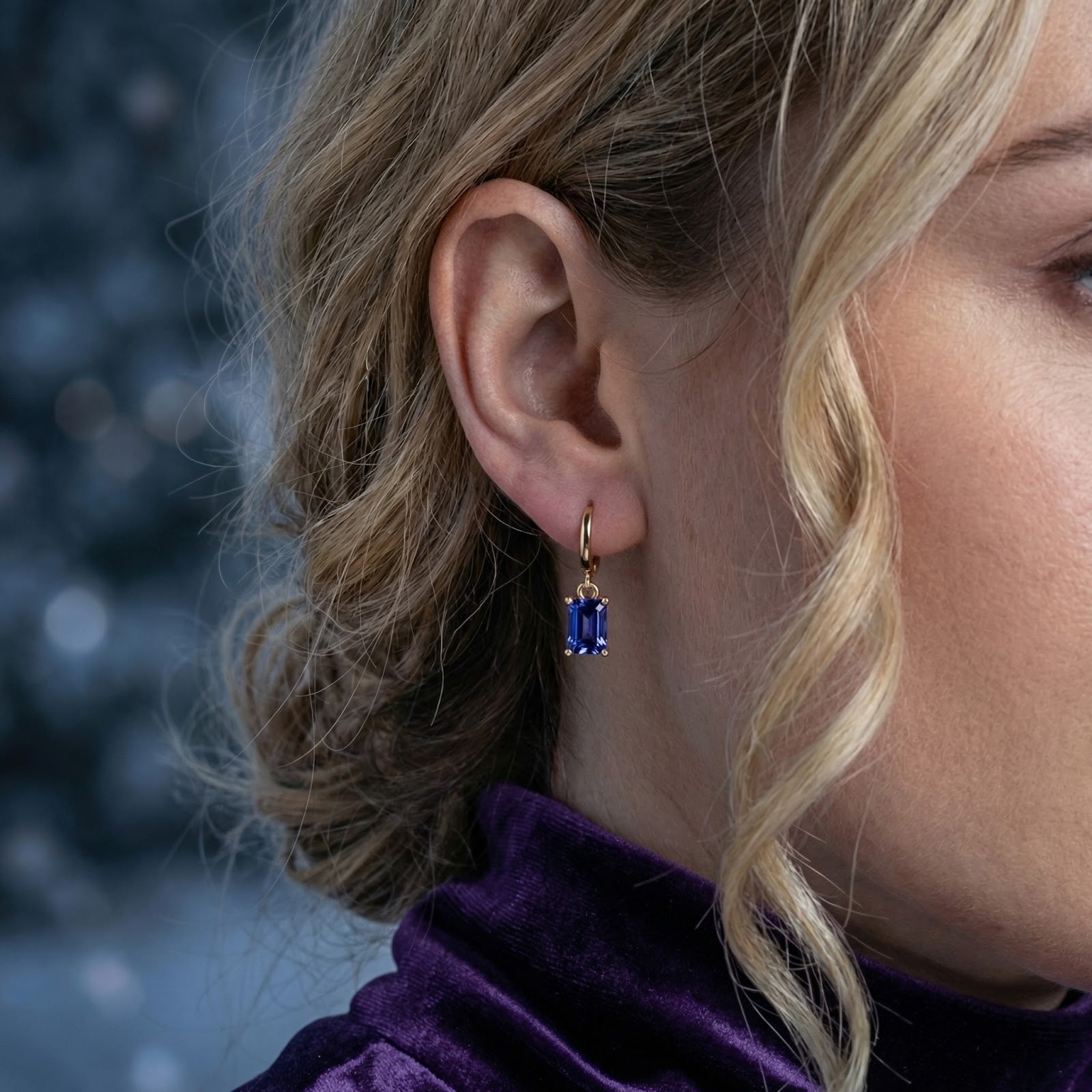 Close-up of a woman wearing an 18K gold vermeil drop earring with an emerald-cut simulated tanzanite stone.