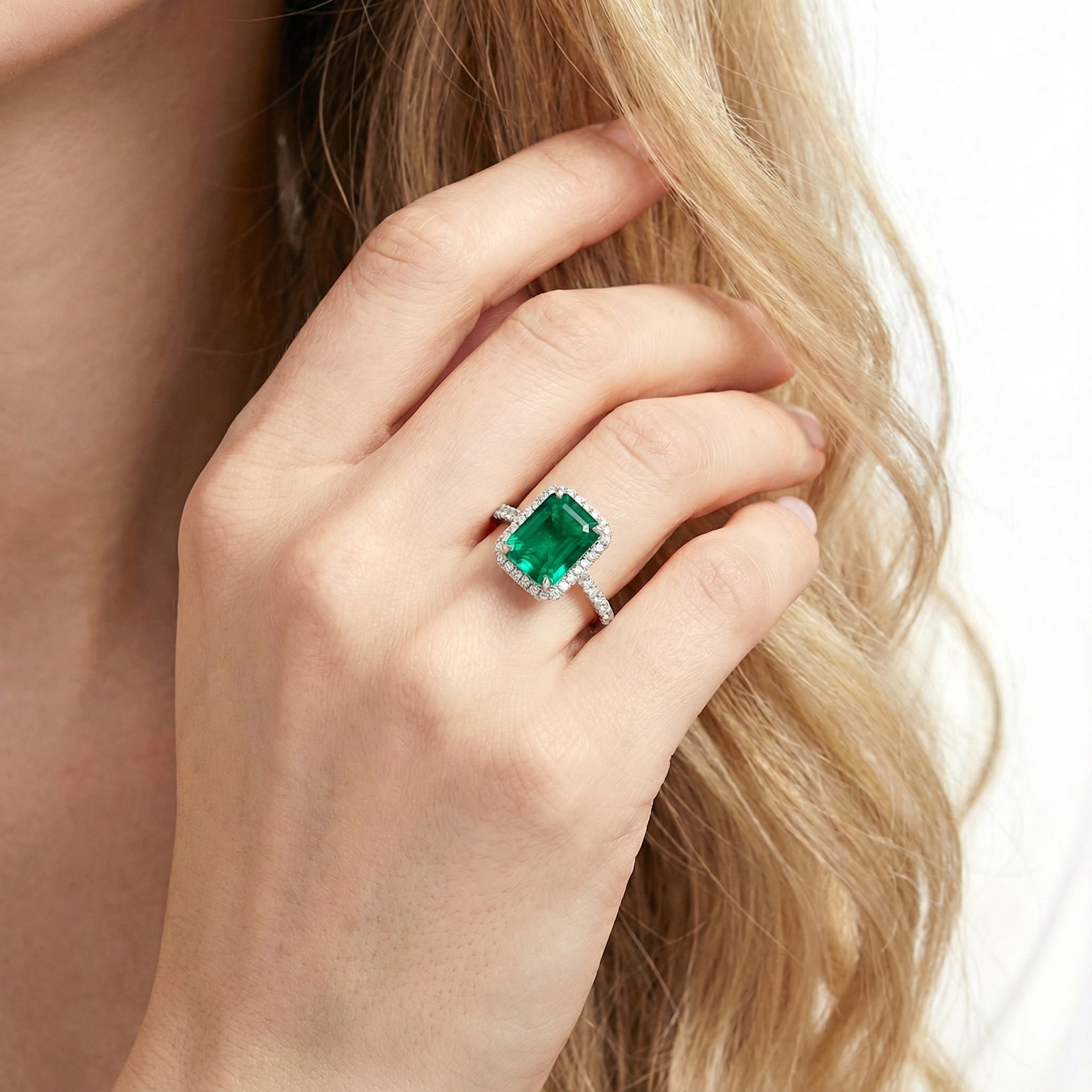 Emerald-cut simulated emerald halo ring in sterling silver worn on a woman's hand against blonde hair.