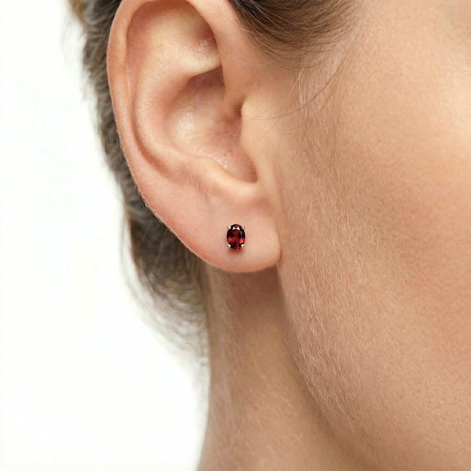 Close-up of an oval cut simulated garnet stud earring in 18K gold vermeil worn on a model's ear.