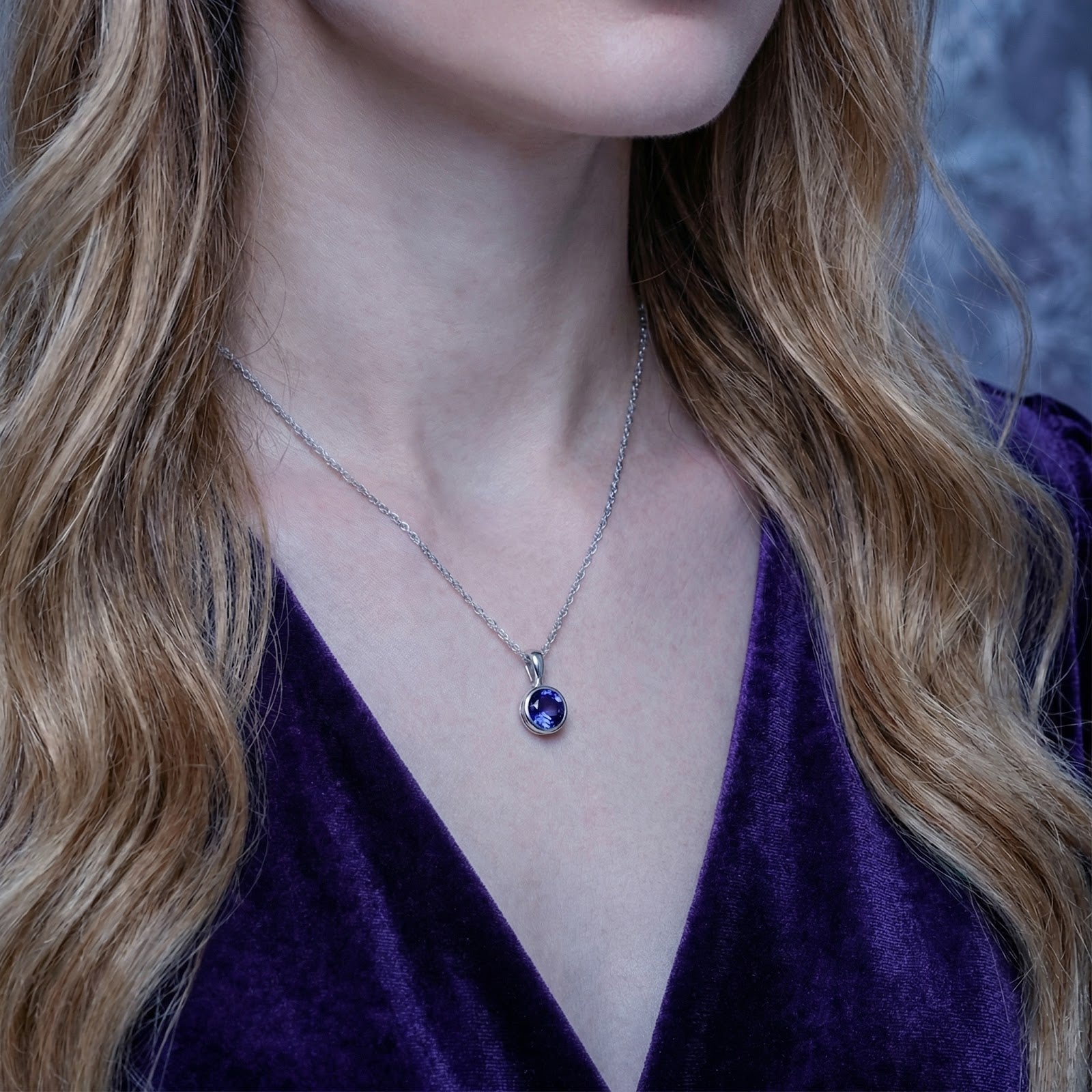 Close-up of a woman wearing the Neriselle round simulated tanzanite solitaire necklace in sterling silver.