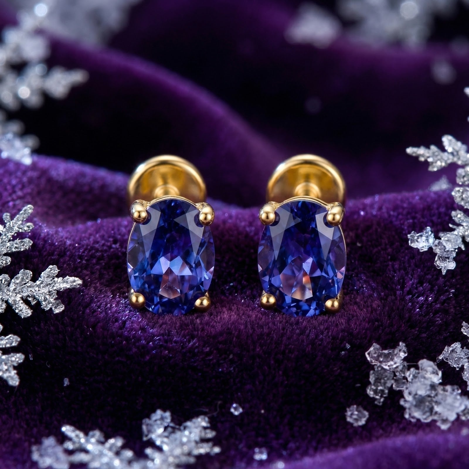 Pair of oval cut simulated tanzanite stud earrings in 18K gold vermeil on a purple velvet background.