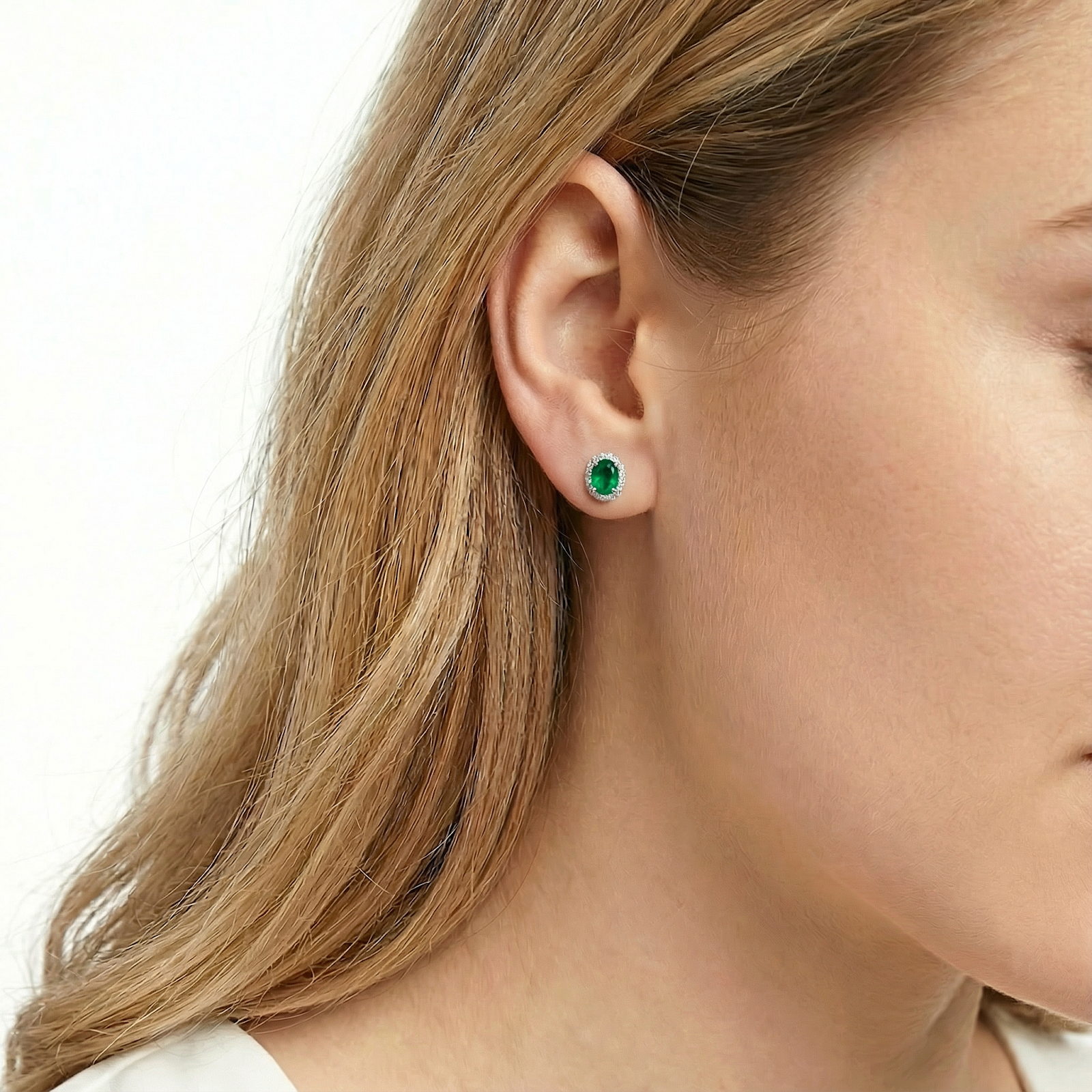 A blonde woman wearing the Solenza oval simulated emerald halo stud earring in S925 sterling silver.