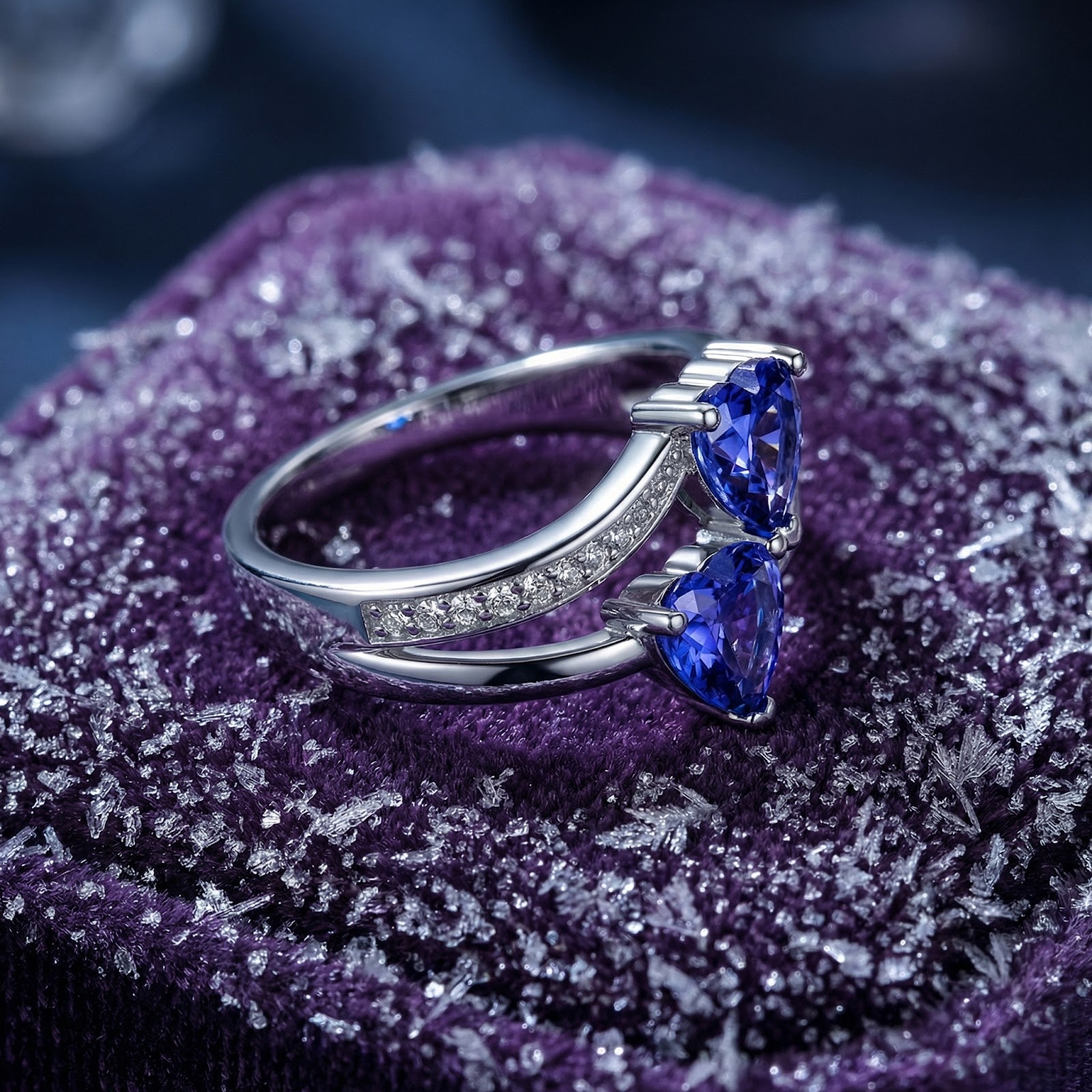 Angled view of the S925 sterling silver heart bypass ring with blue heart-cut simulated tanzanite on purple velvet.