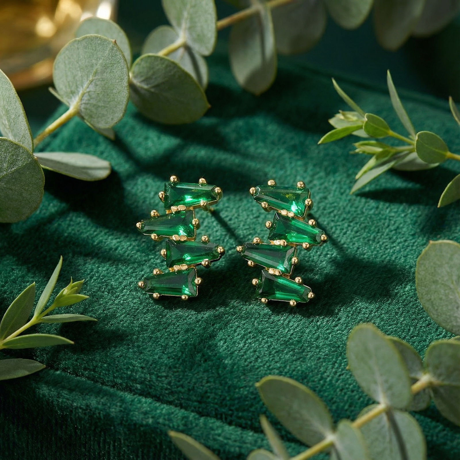 Pair of 18K gold vermeil geometric taper simulated emerald earrings displayed on a green velvet jewelry box.