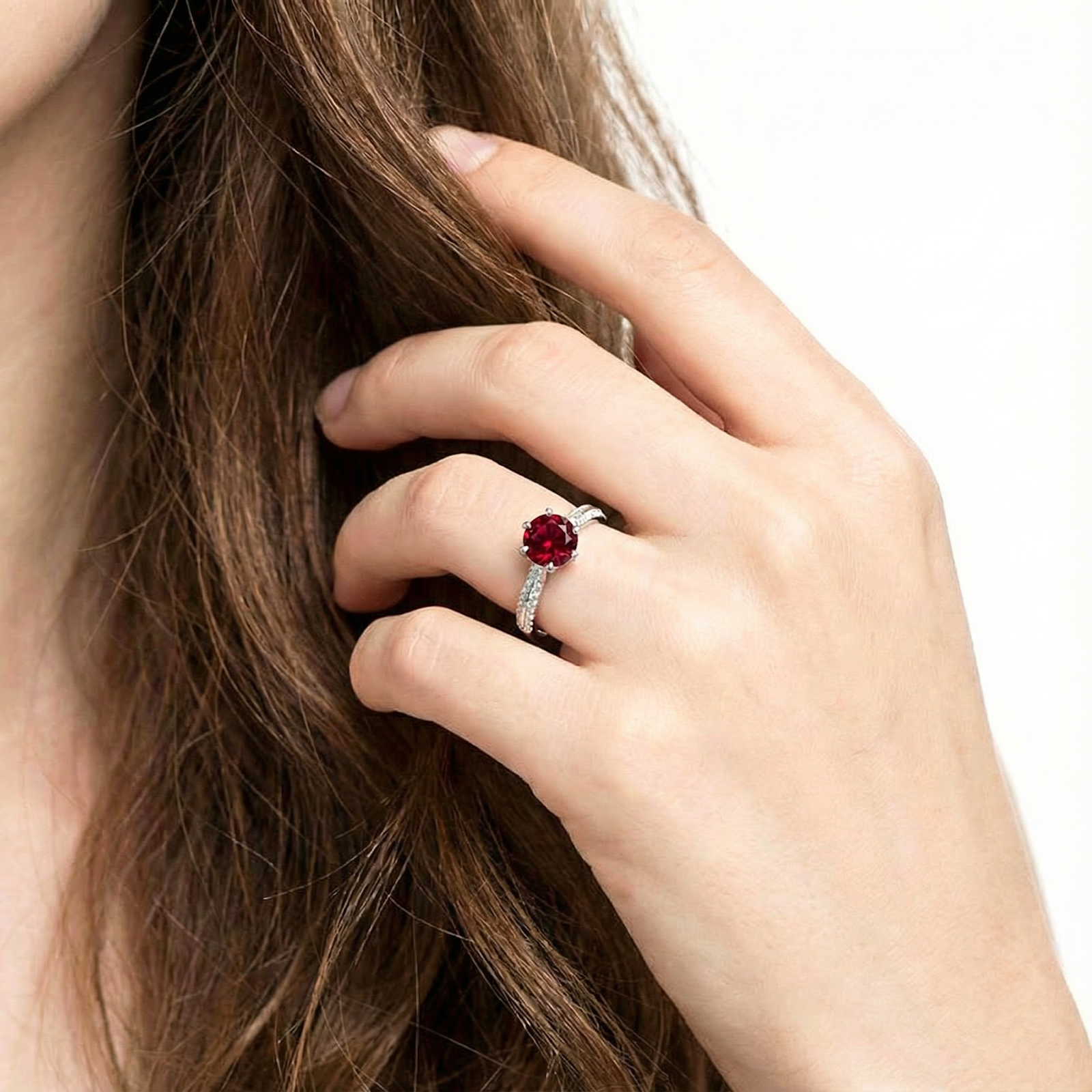 Round cut simulated ruby solitaire ring in sterling silver worn on a hand touching long brown hair.