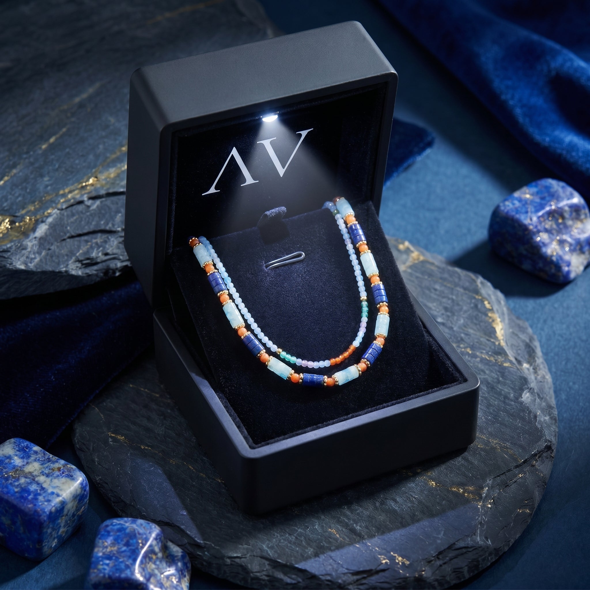 The Cobalt Strands lapis necklace presented in a premium black LED-lit jewelry gift box on a stone surface.